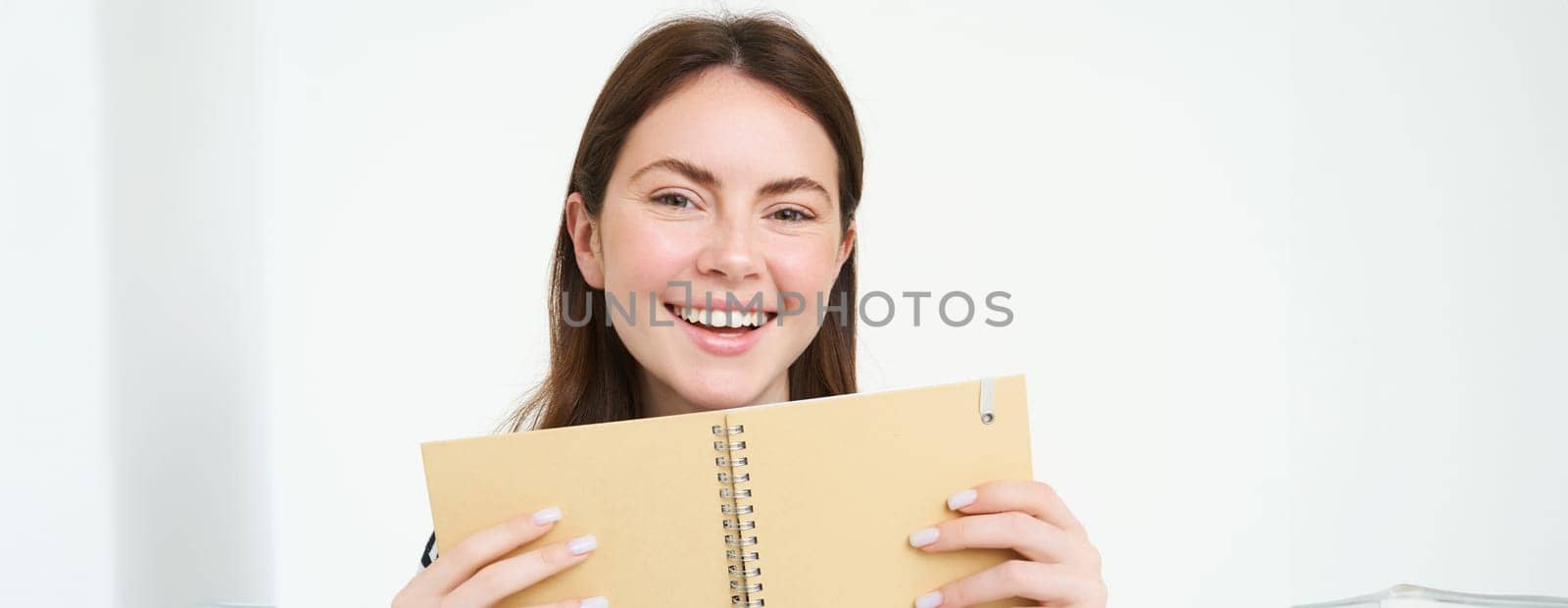 Portrait of happy woman smiling, showing her book, daily planner, holding notebook, planning her trip an writing notes in organizer, isolated against white background.