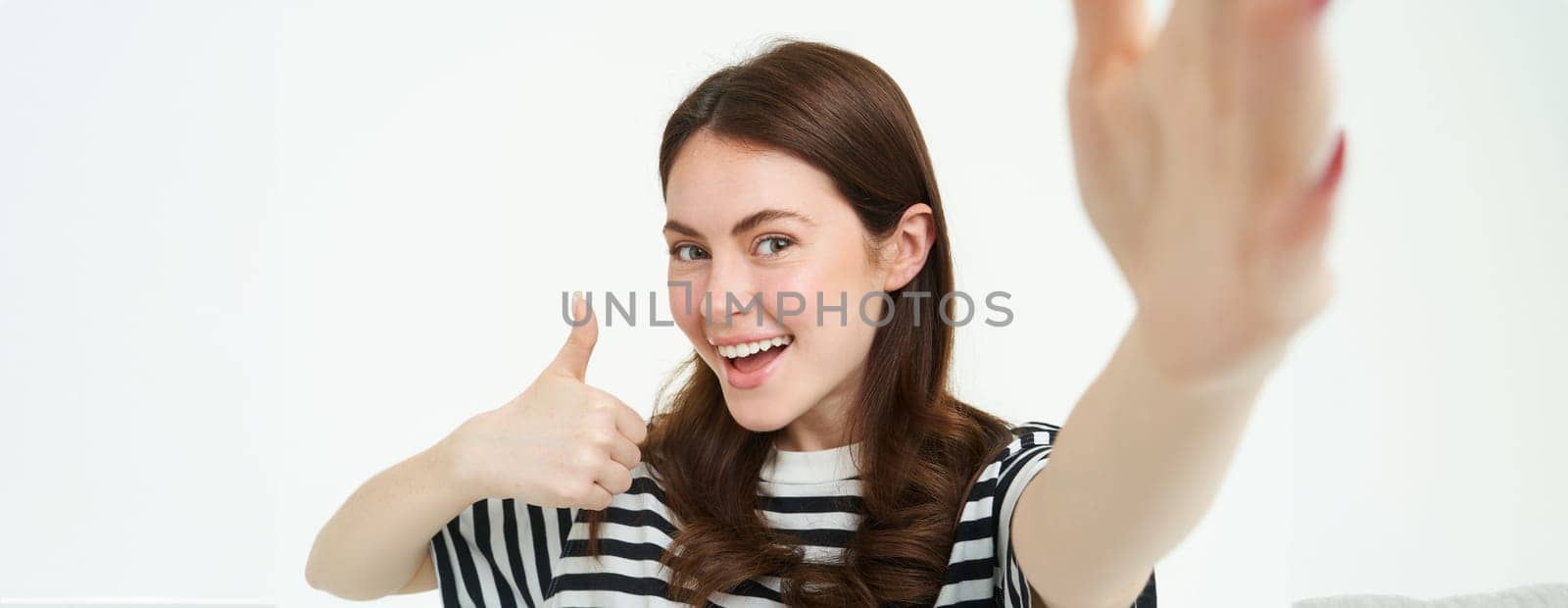 Portrait of smiling woman recommending product, shows thumbs up, takes selfie with something good, copy space, standing isolated on white background,