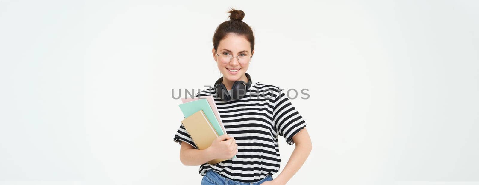 Portrait of smiling, confident young woman, holding notes, notebooks in her hands, going to college, student posing against white background.