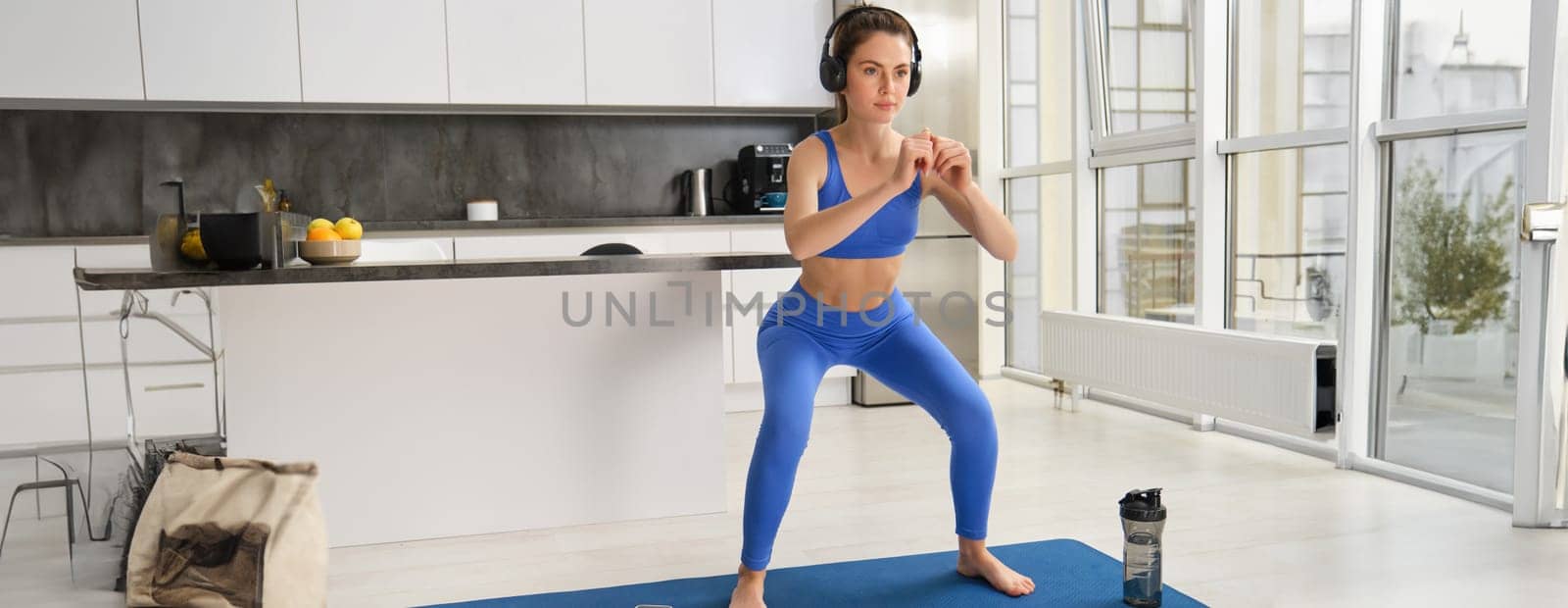 Portrait of young woman doing aerobics exercises in living room, sport training at home, standing on rubber fitness mat and doing workout.