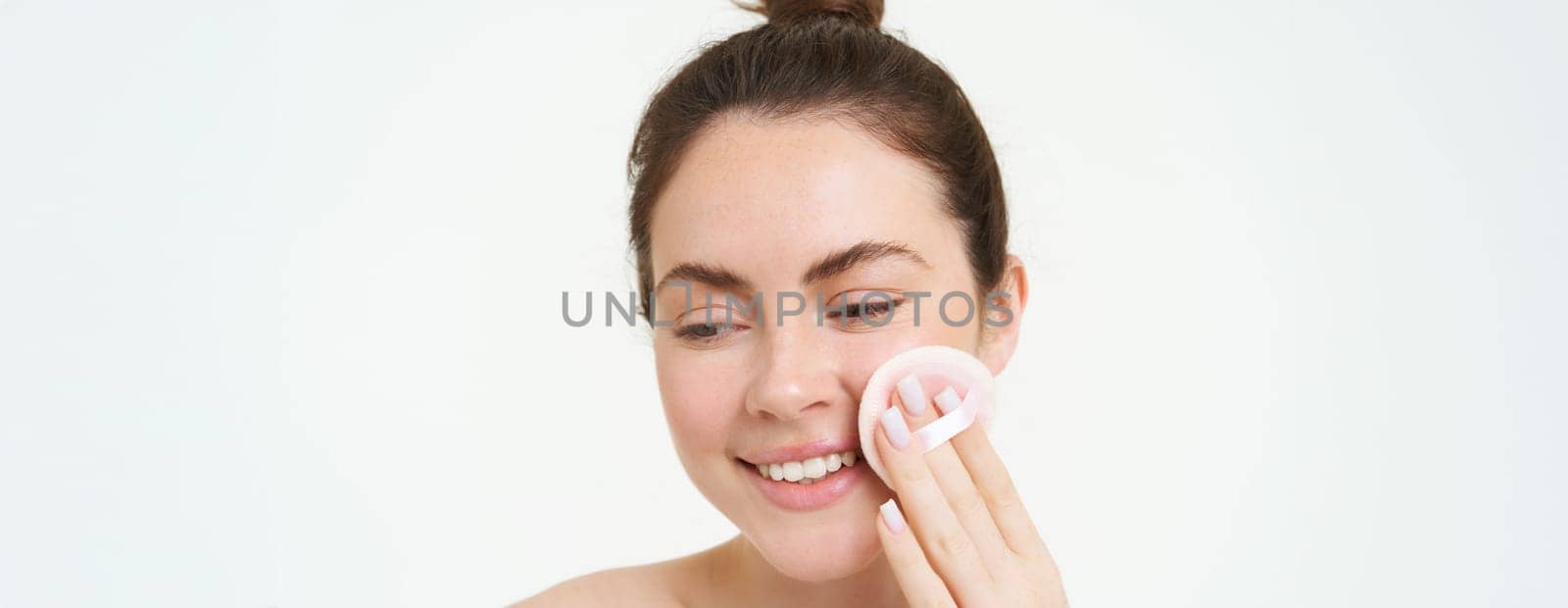 Portrait of young woman cleansing her face, takes off her makeup, washing her face, using skincare routine with cotton pads, isolated over white background.