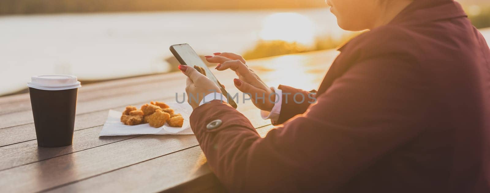 Banner muslim woman in hijab using smartphone outdoor tasty nuggets and coffee background, close up. Street food and picnic in spring morning by Satura86