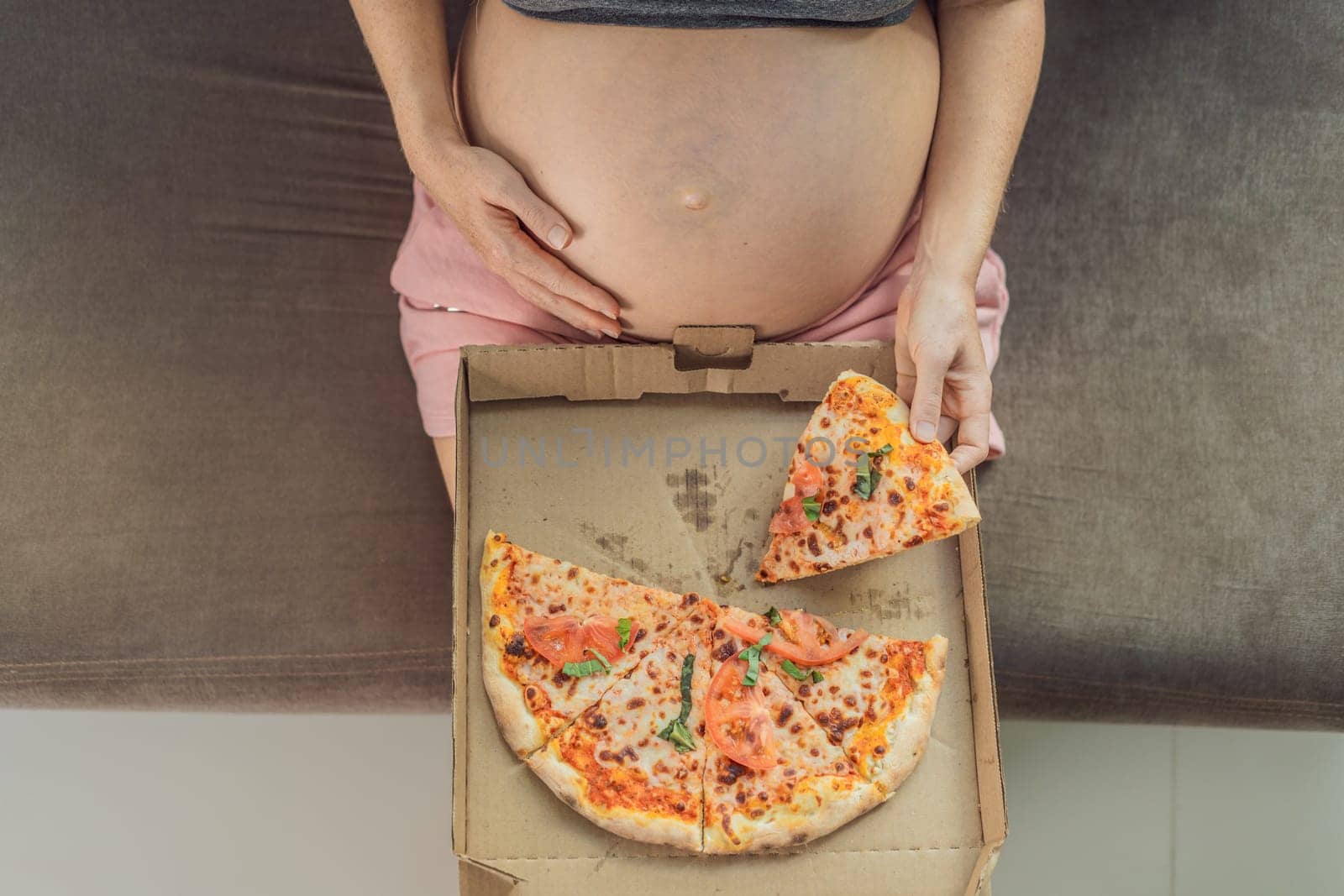 A pregnant woman enjoys a slice of pizza, savoring a moment of indulgence while satisfying her craving for a delightful, comforting treat. Excited Pregnant Young Lady Enjoying Pizza Holding Biting Tasty Slice Posing With Carton Box. Junk Food Lover Eating Italian Pizza. Unhealthy Nutrition Cheat Meal.