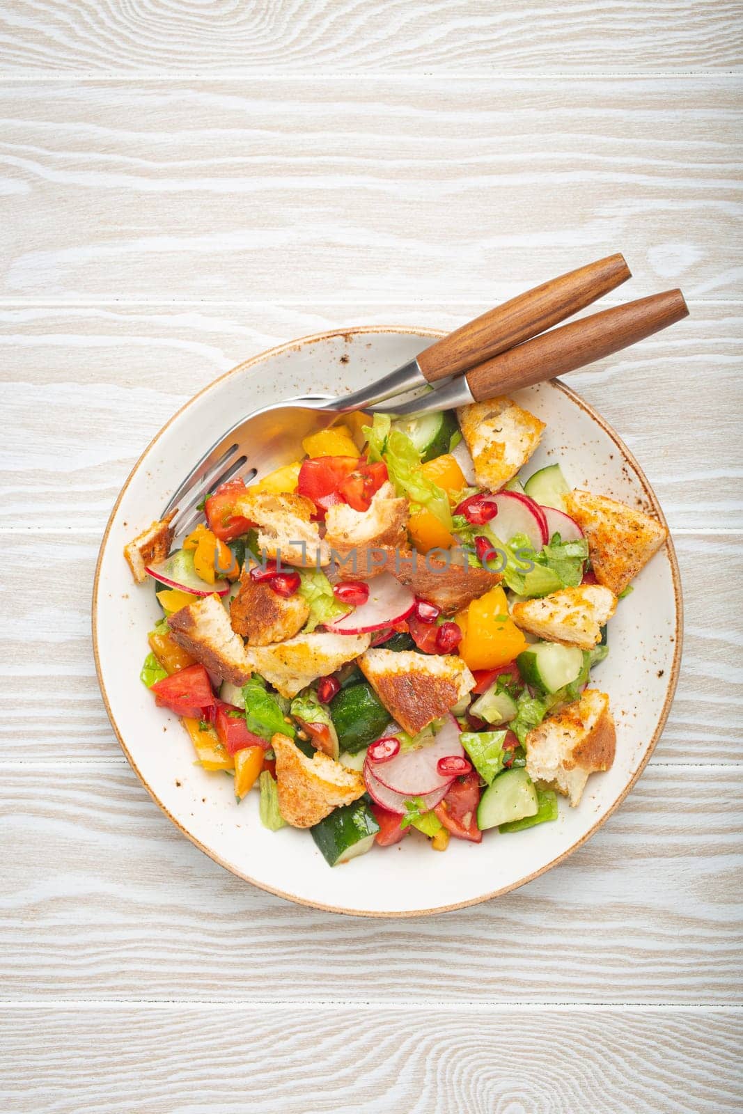 Traditional Levant dish Fattoush salad, Arab cuisine, with pita bread croutons, vegetables, herbs. Healthy Middle Eastern vegetarian salad, rustic wooden white background top view by its_al_dente