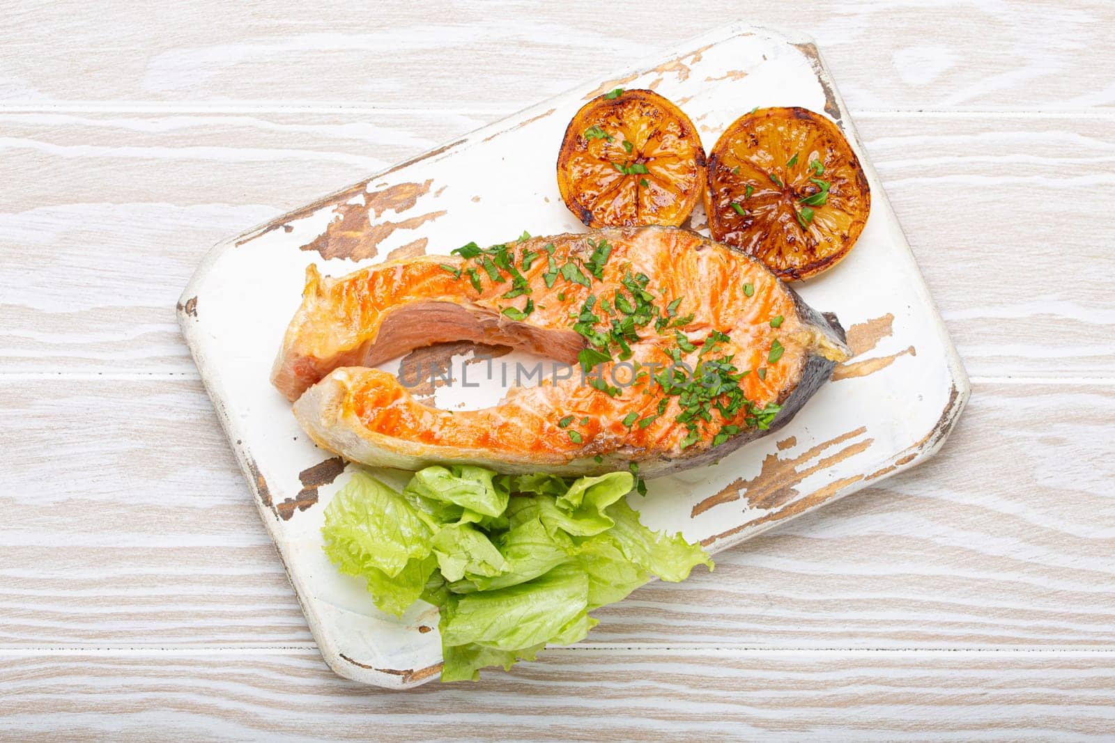 Grilled fish salmon steak and green salad with lemon served on white cutting board rustic wooden background top view, balanced diet or healthy nutrition meal with salmon and veggies.