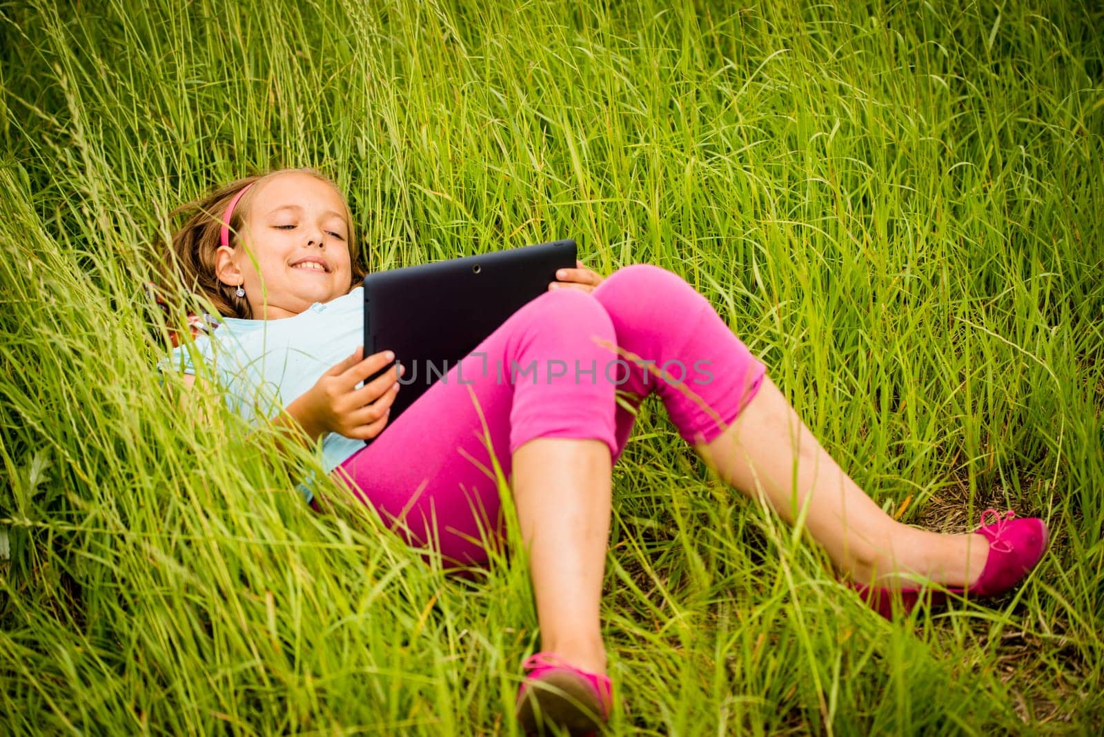 Smiling teen girl lying in grass and watching tablet