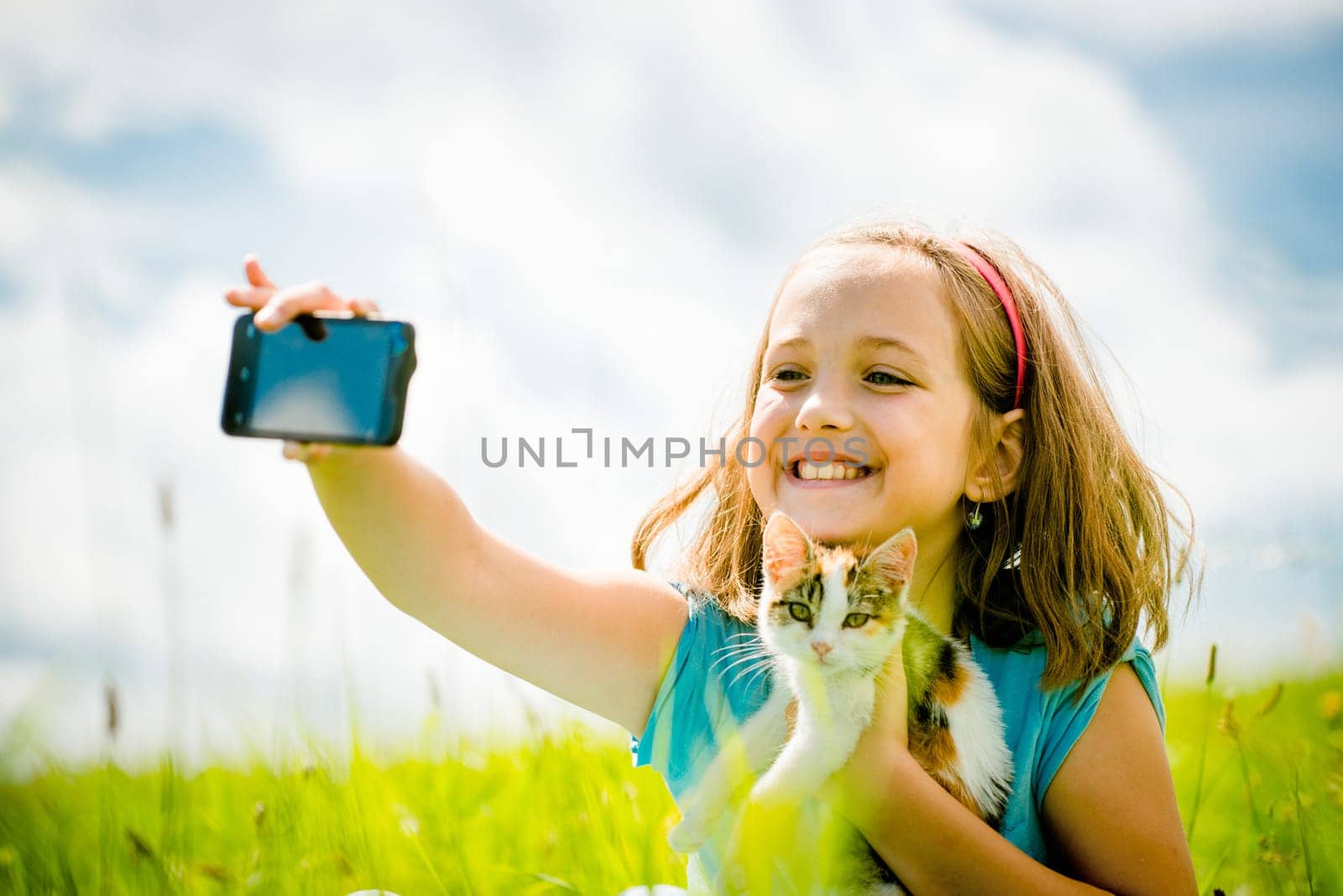 Child taking photo with mobile phone camera of herself and her cat - outdoor in nature