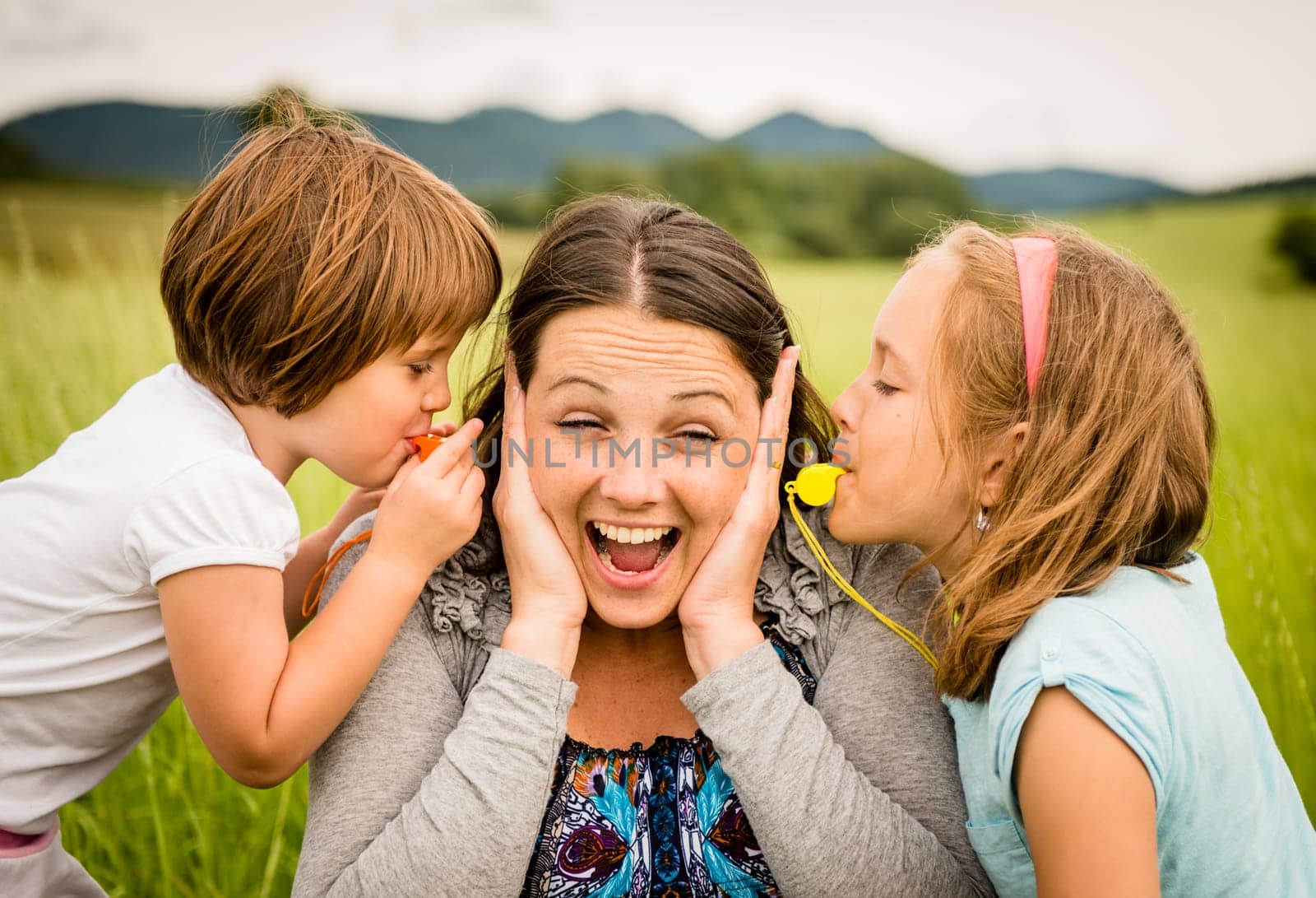 Children blowing whistles to mother's ears- outdoor in nature