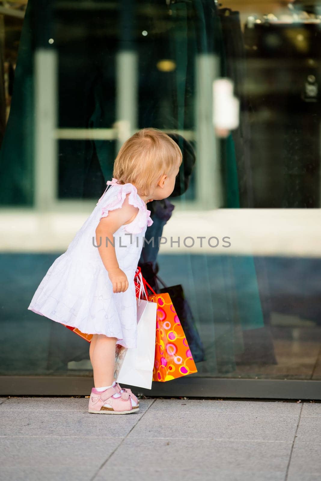 Little girl in white dress looking through shop window