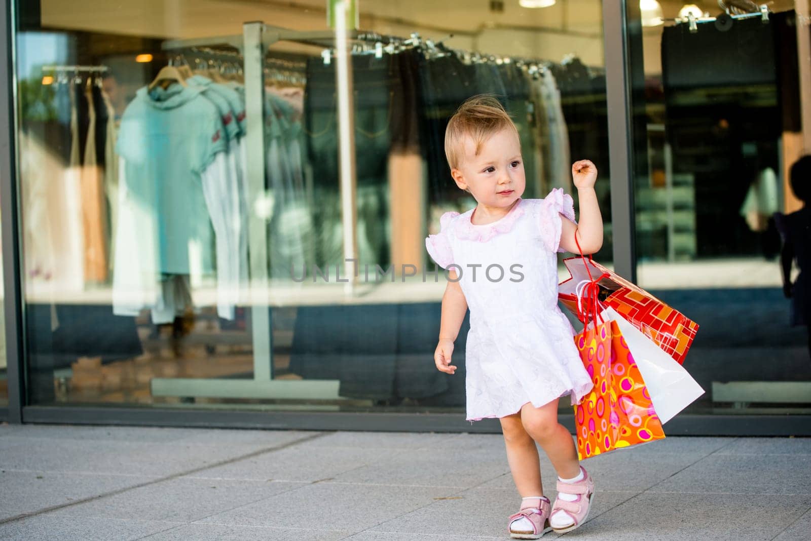 Cute baby goes shopping with bags, shops in background