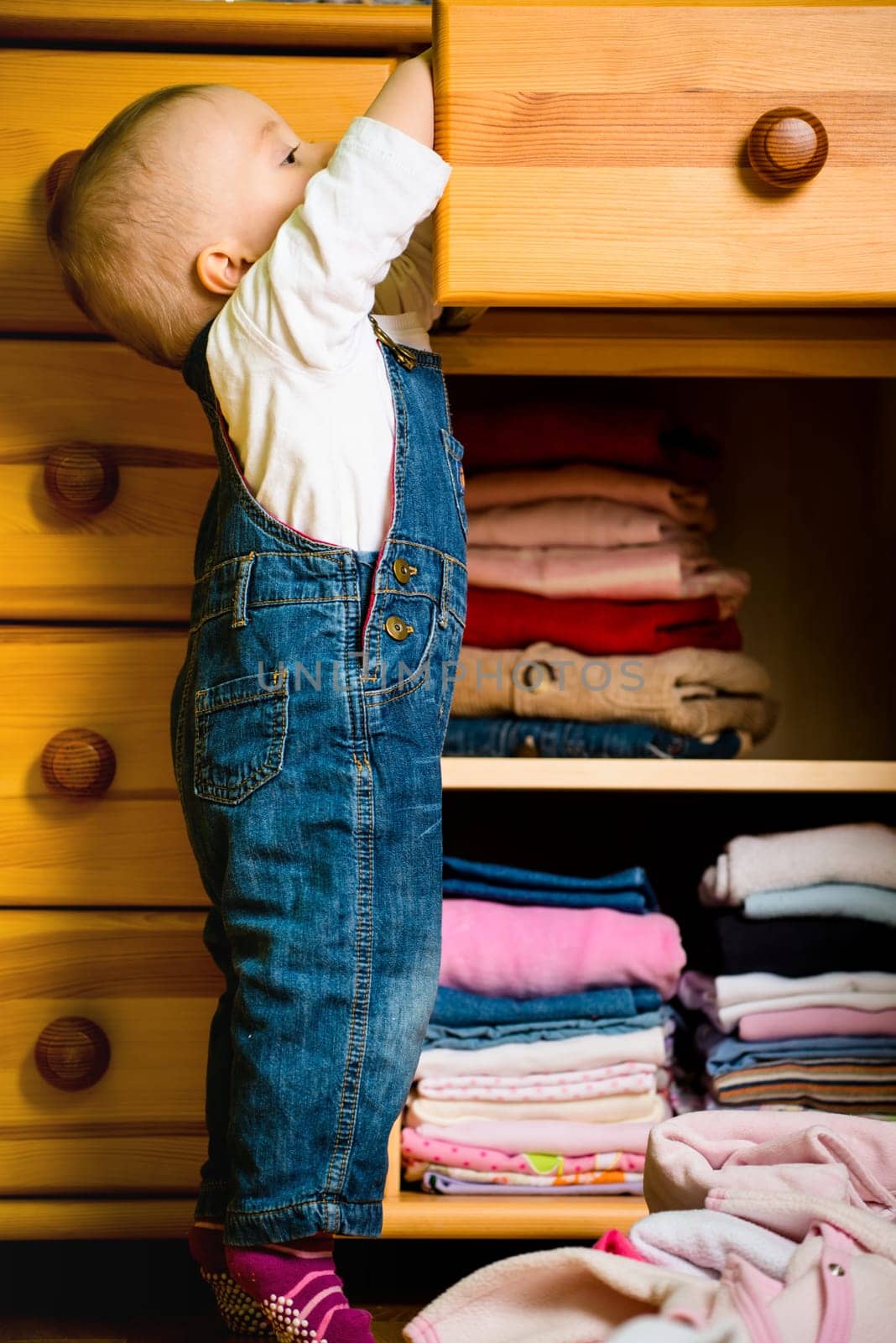 Baby throws out clothes from wooden furniture at home