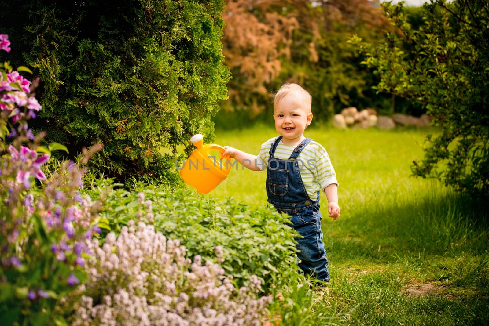 Little baby girl waters plants in backyard garden with watering can
