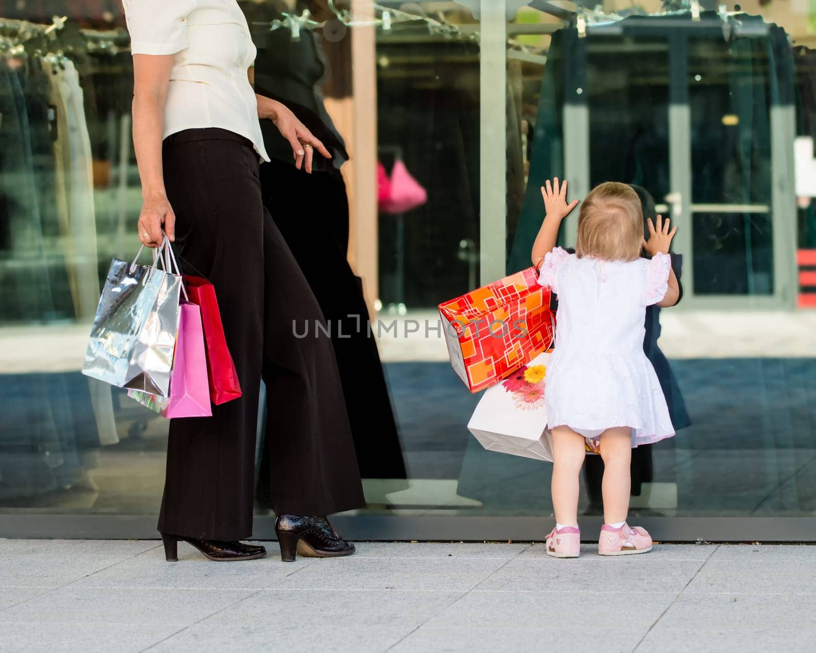 Mother with little girl in white dress looking through shop window
