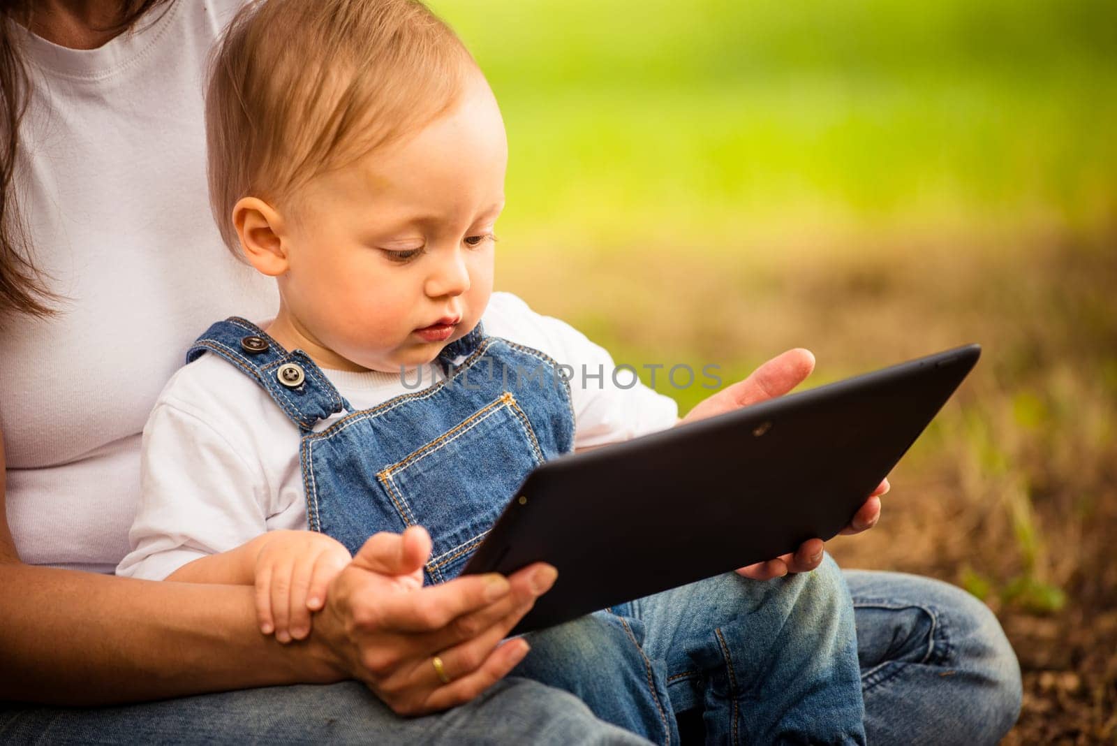 Mother with her baby watching together in tablet computer outdoor
