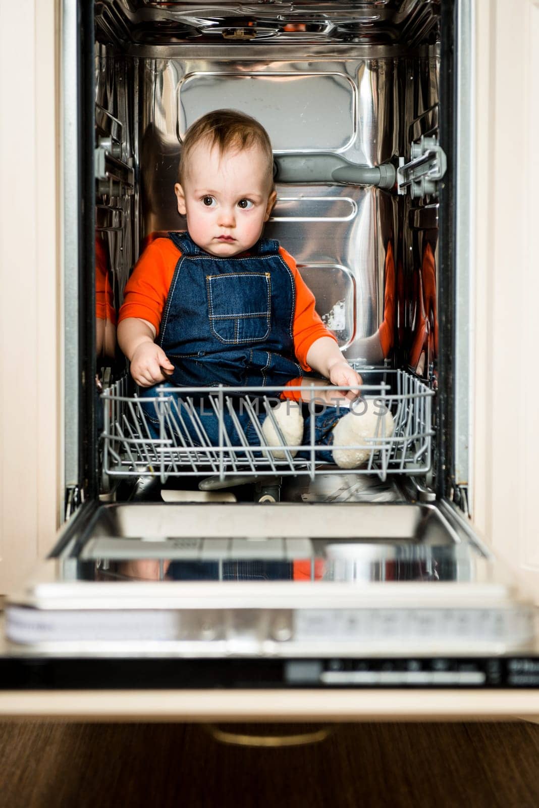 Cute baby sitting in empty dishwasher with tablet