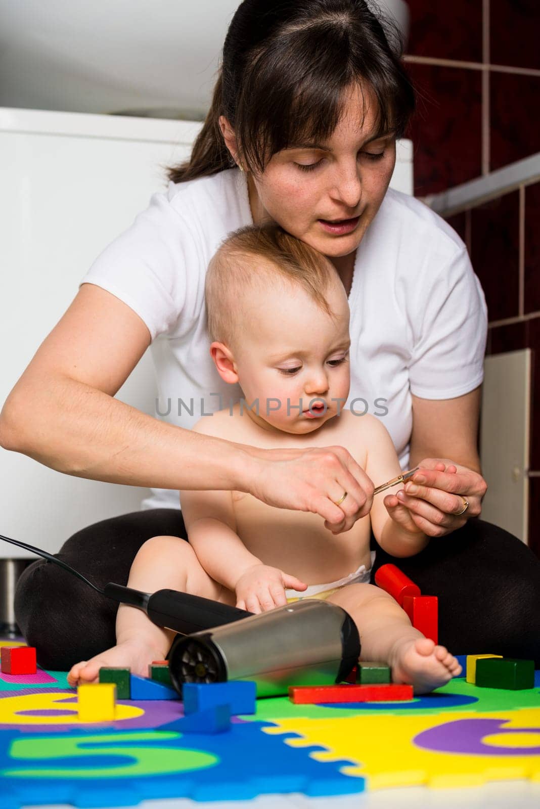 Mother cutting fingernails of her child while baby is playing with toys