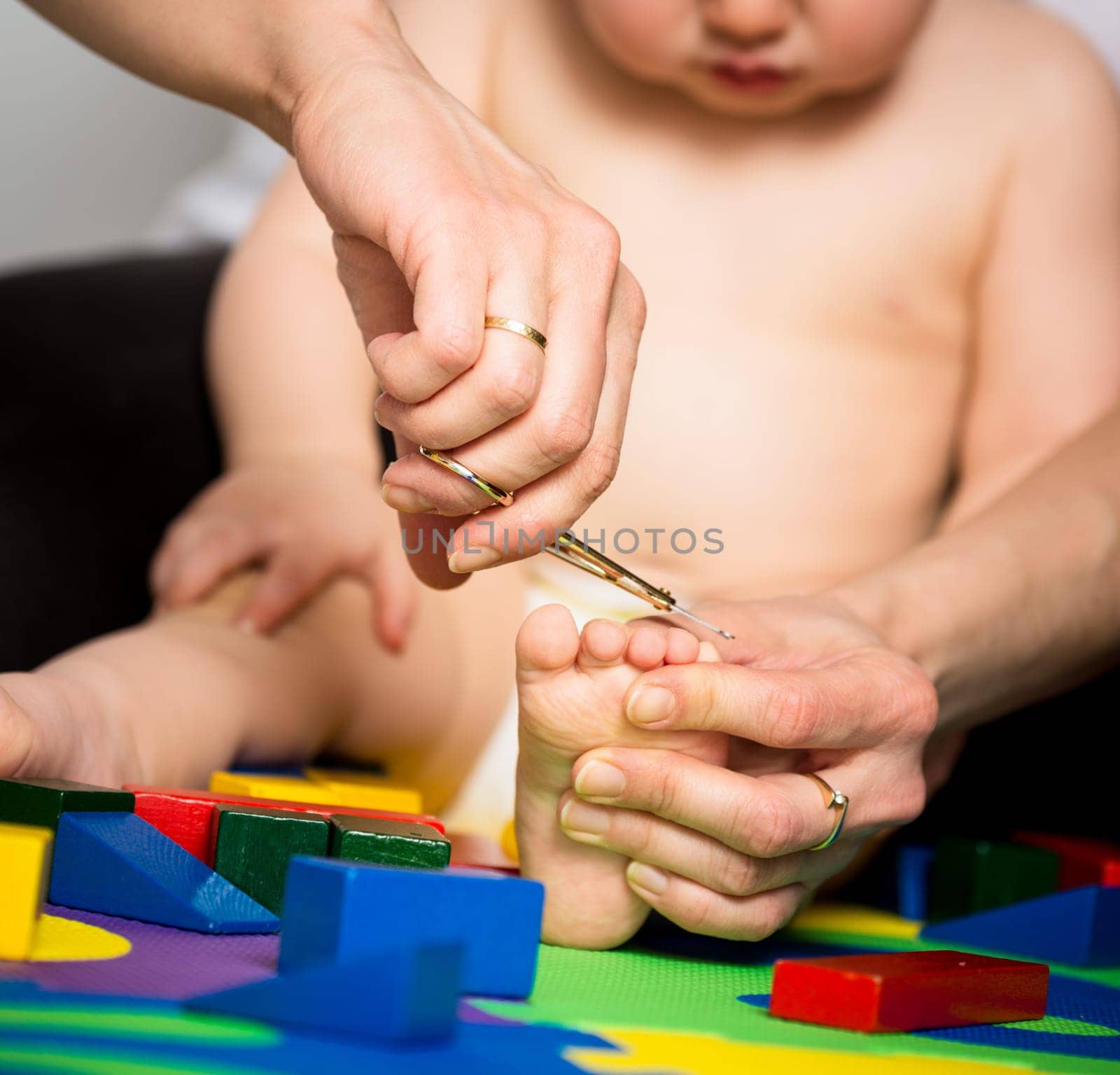 Mother trimming toenails on feet of her baby - toys around
