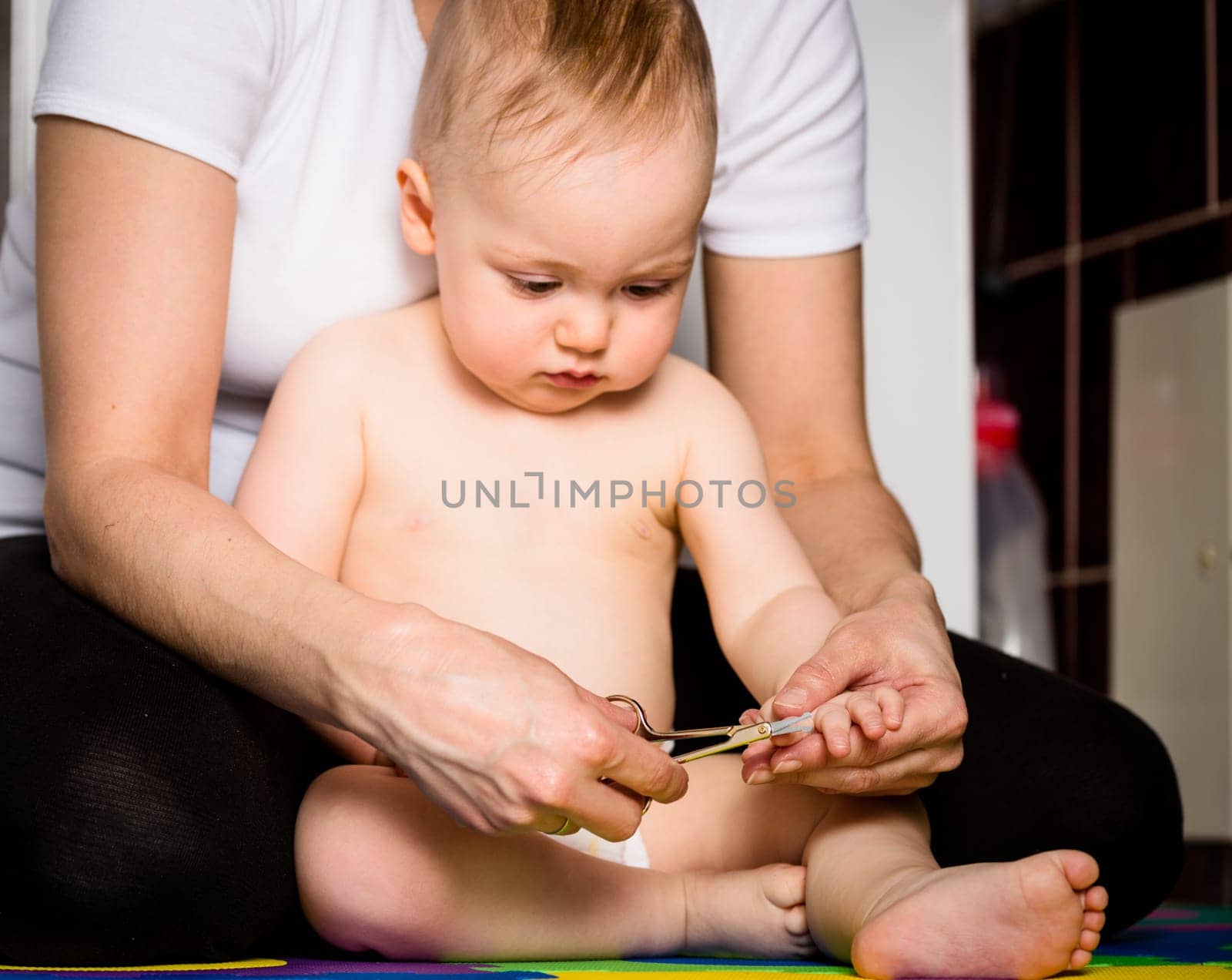 Mother cutting nails on hands of her baby - sitting on floor in bathroom