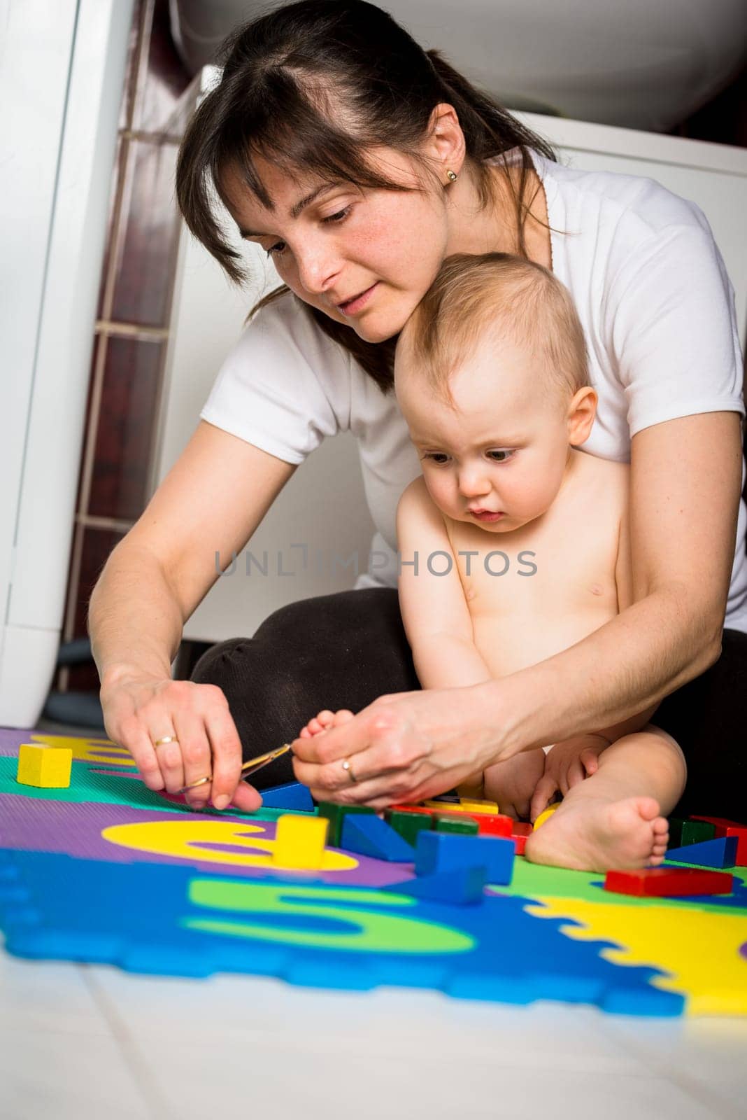 Mother cutting nails on feet of her baby - sitting on floor in bathroom
