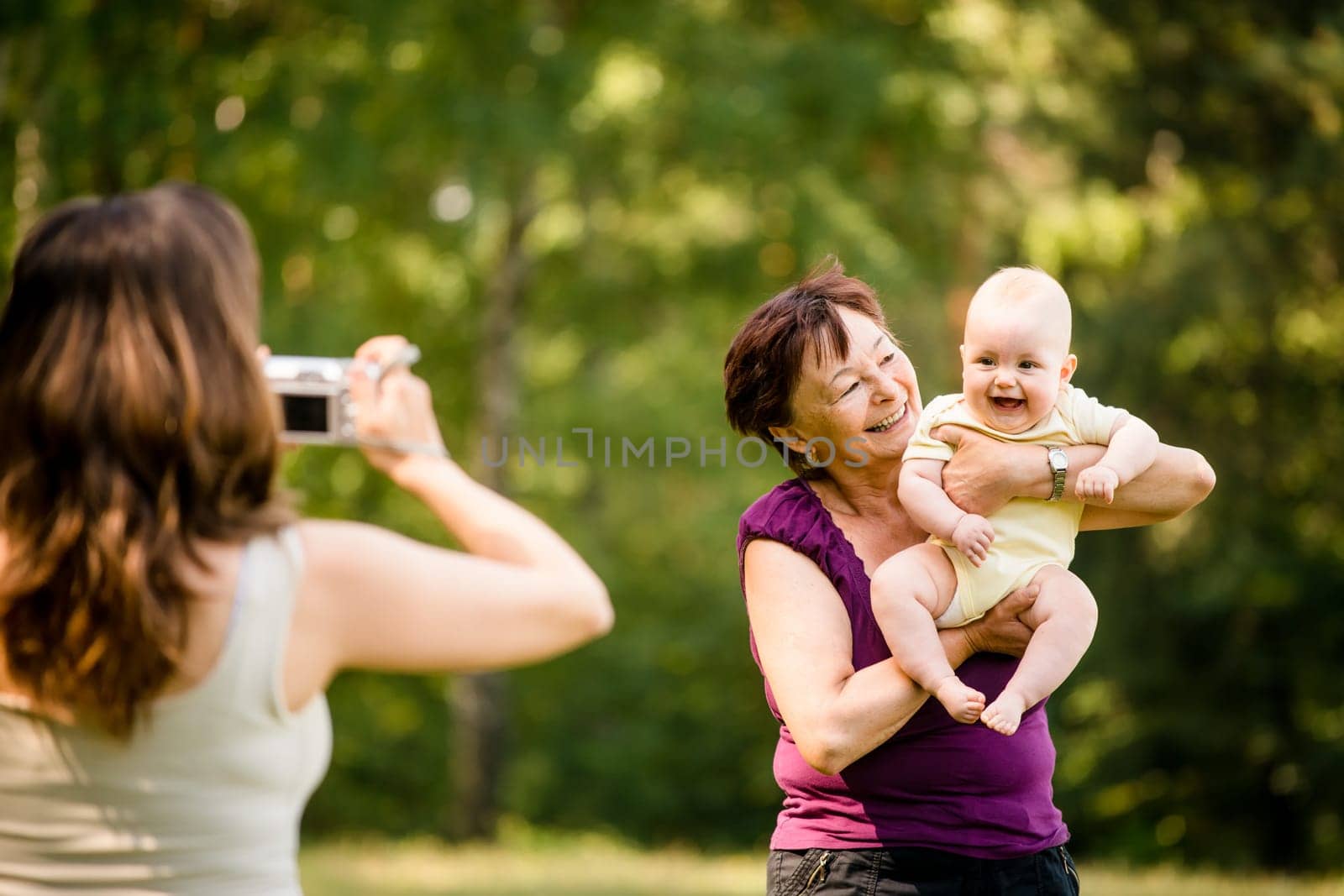 Mother taking photo of grandmother holding her granddaughter - outdoor in nature