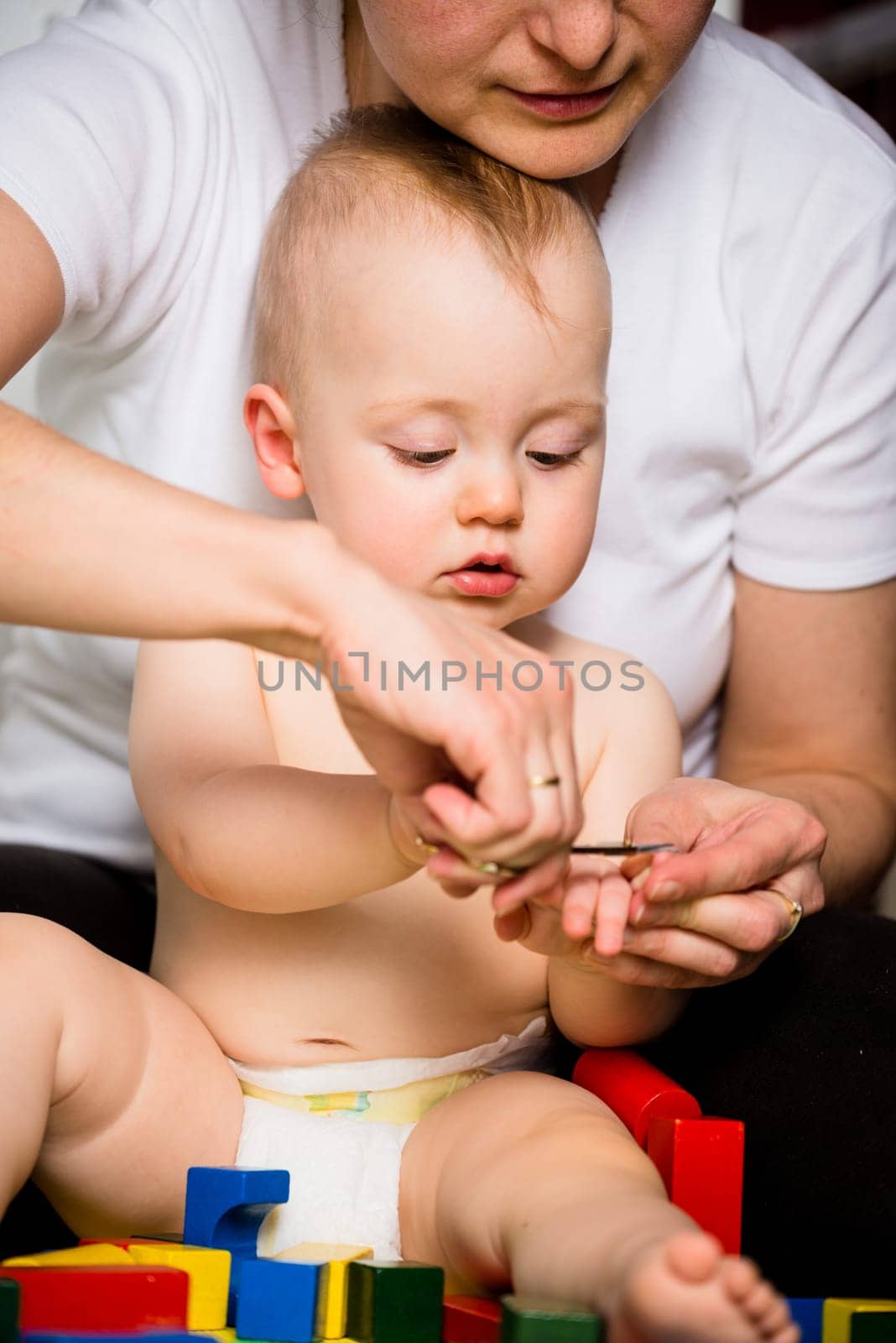 Mother cutting nails on hands of her baby - sitting on floor in bathroom