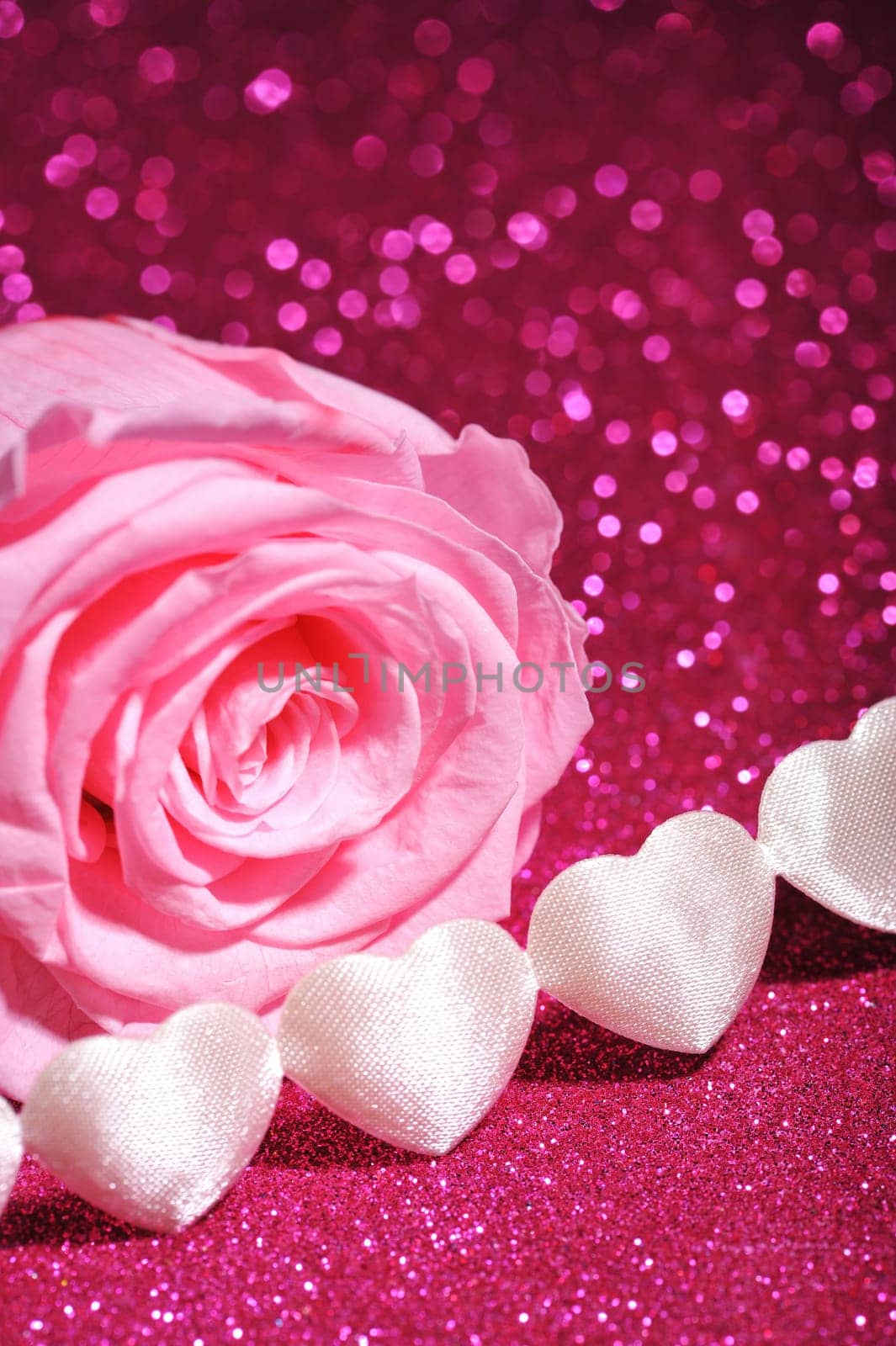 Chain of white fabric hearts with pink rose on pink glitter background