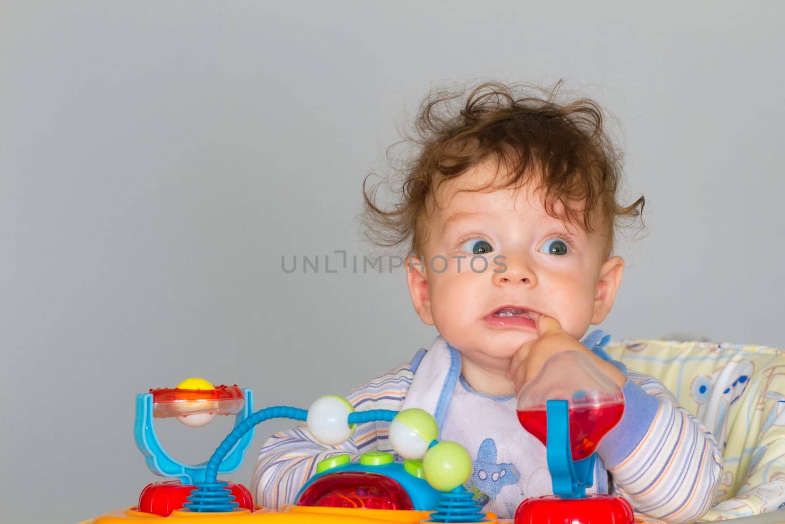 7 months old baby boy portrait while in walker with finger in his mouth.