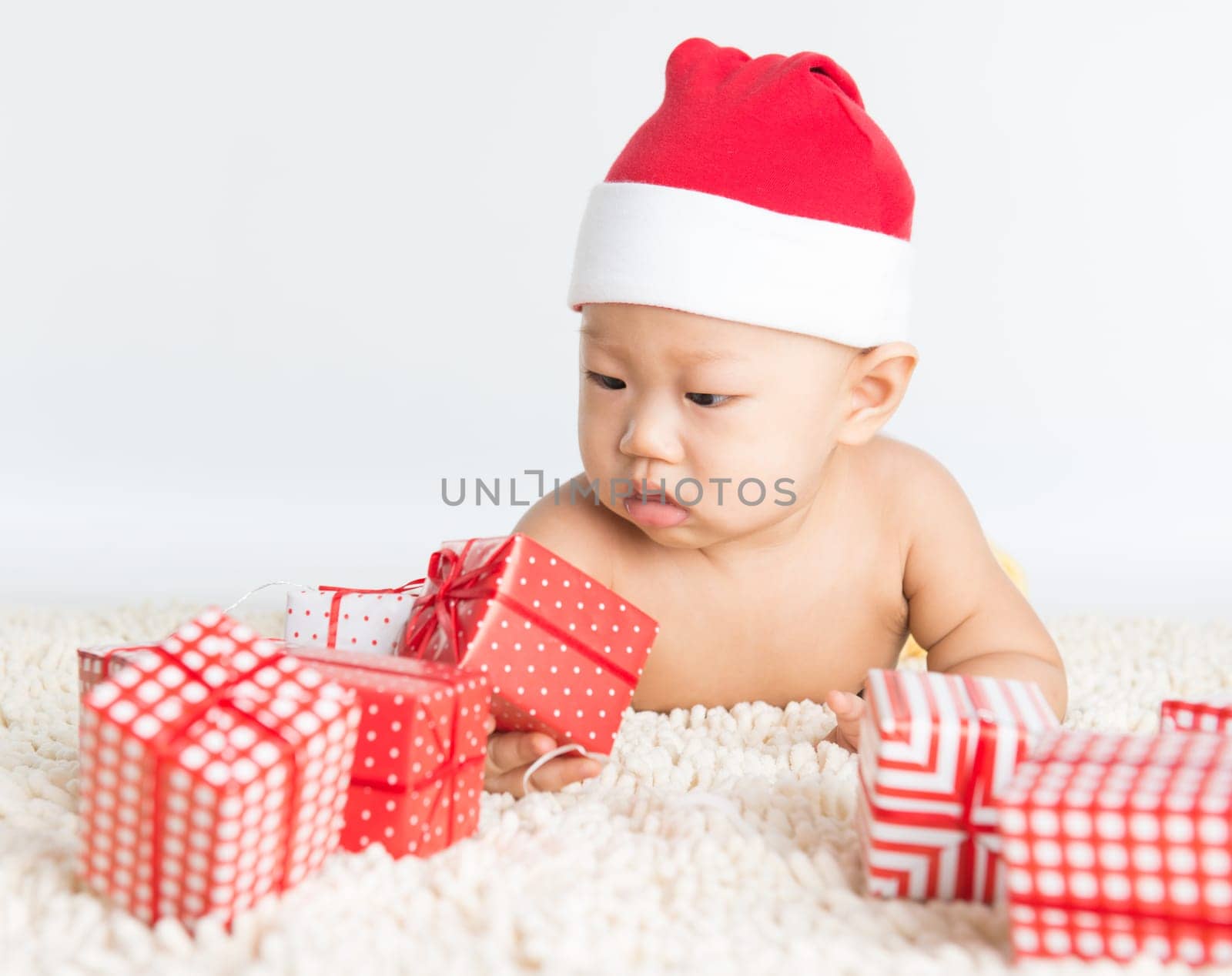 Asian baby boy with santa hat playing with Christmas present on floor.
