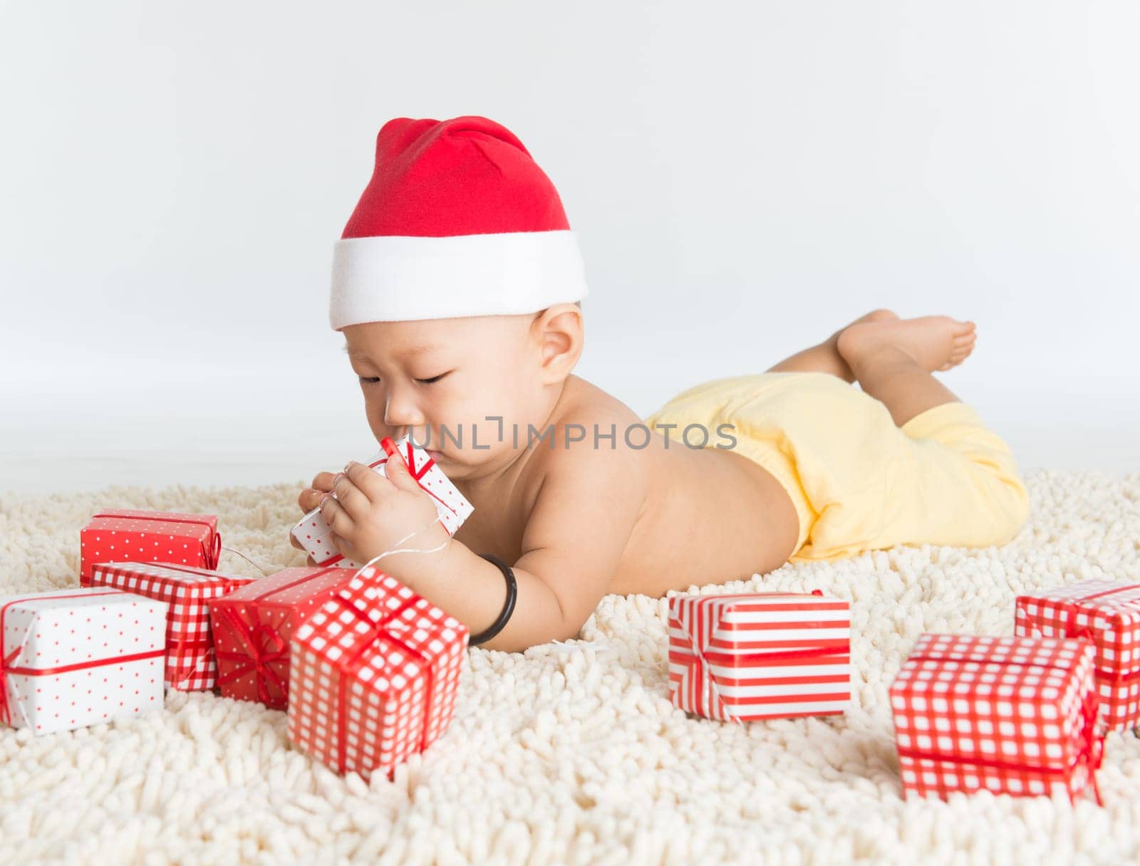 Asian baby boy with santa hat playing with Christmas present on floor.