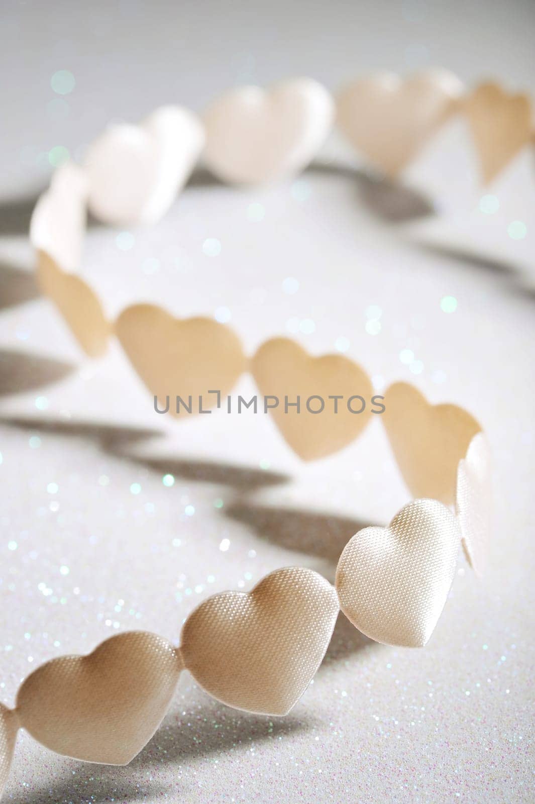 Chain of white yellow fabric hearts on silver glitter background