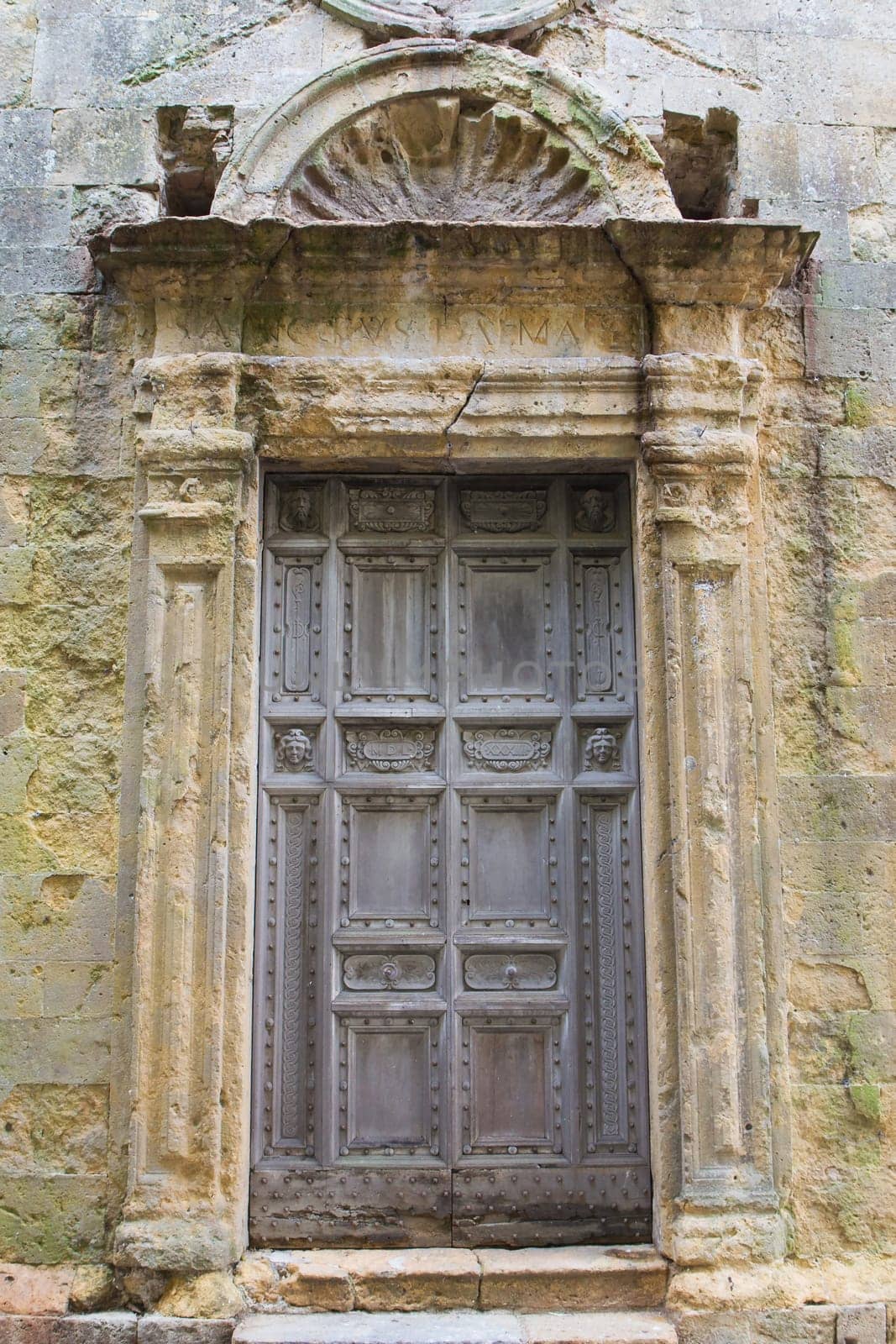 Ancient wooden church door surrounded by weathered plaster.