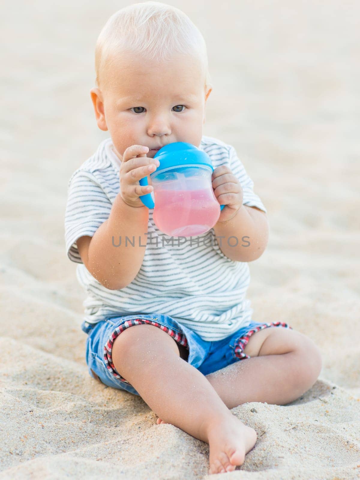 Cute baby sitting on a sand and drinking