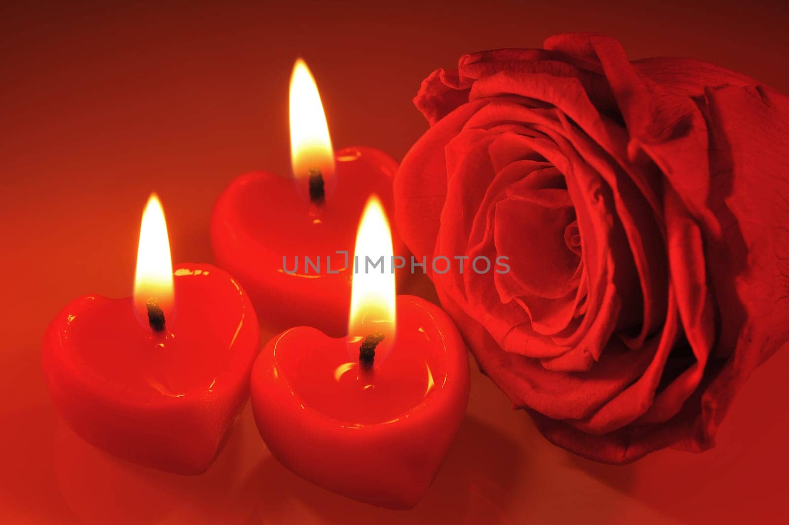 Three luminous candles in heart shape with red rose