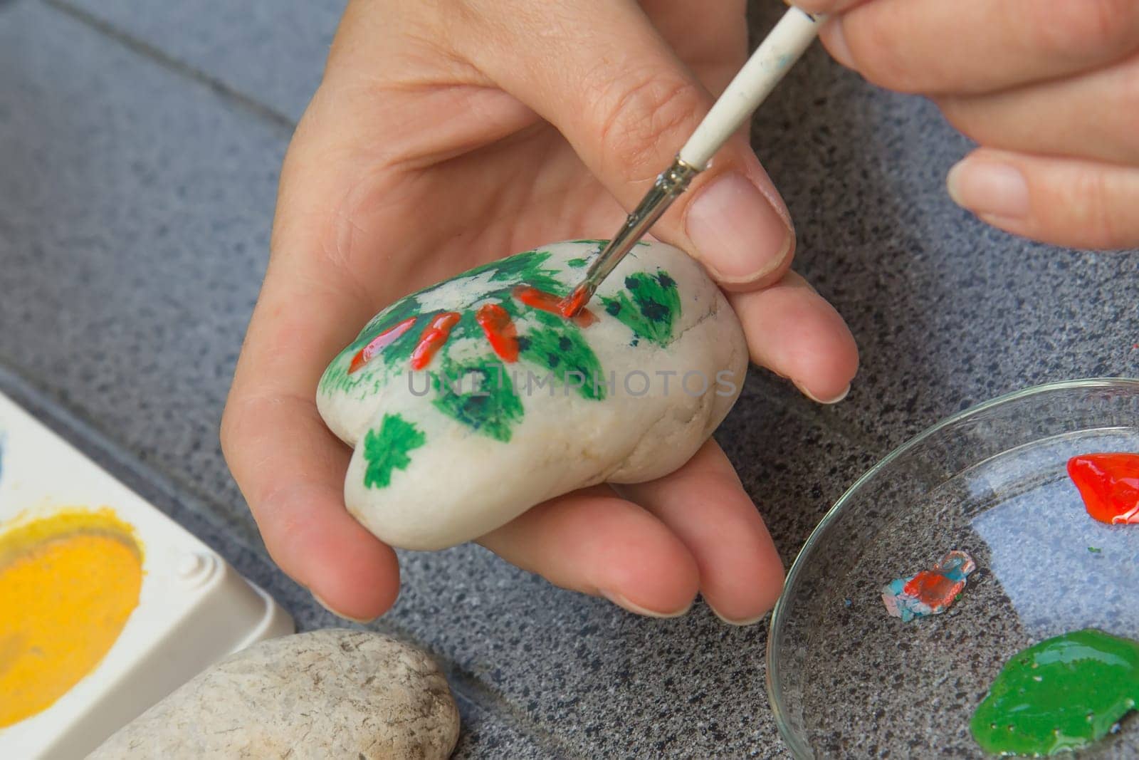 Handmade - stone painting. production decoration. Female hand are drawing picture on the stone.