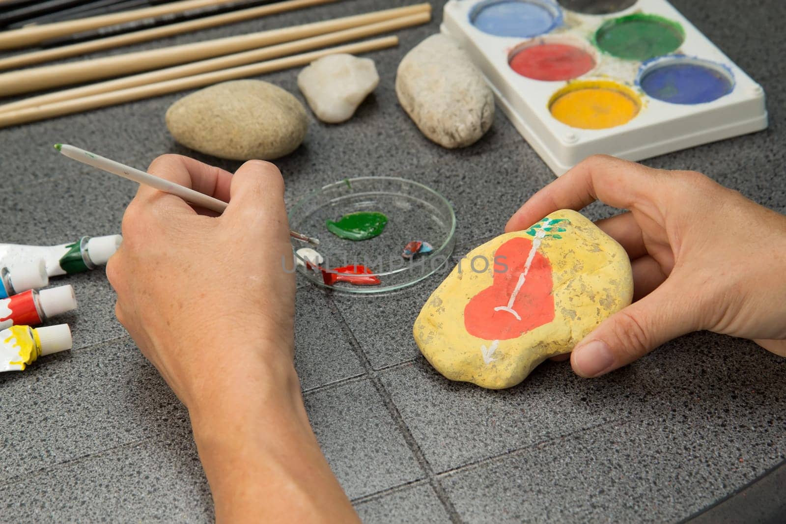 Handmade - stone painting. production decoration. Female hand are drawing red heart on the stone. Horizontally.
