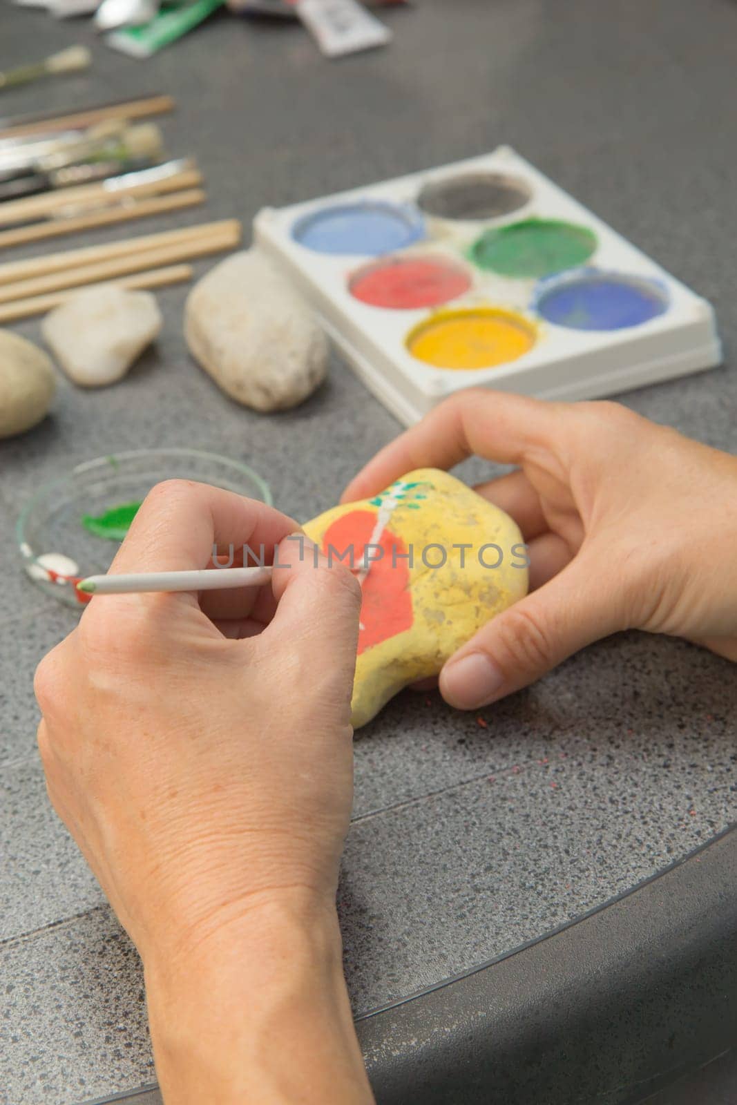 Handmade - stone painting. production decoration. Female hand are drawing red heart on the stone. Vertically.