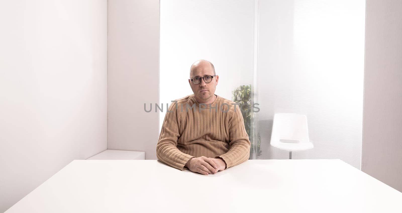 sad bald plump man with glasses in an empty office waiting for something that have to happen