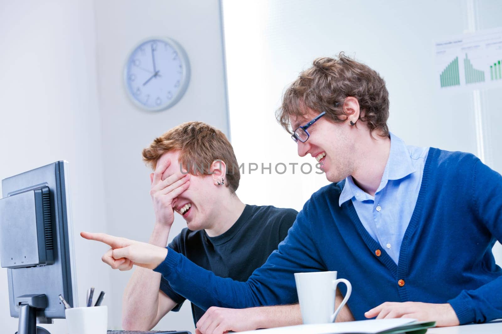 a couple of two young office workers laugh at what is happening on the screen