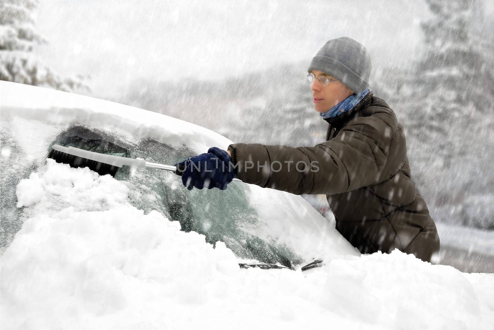 Young man removes the snow from his vehicle