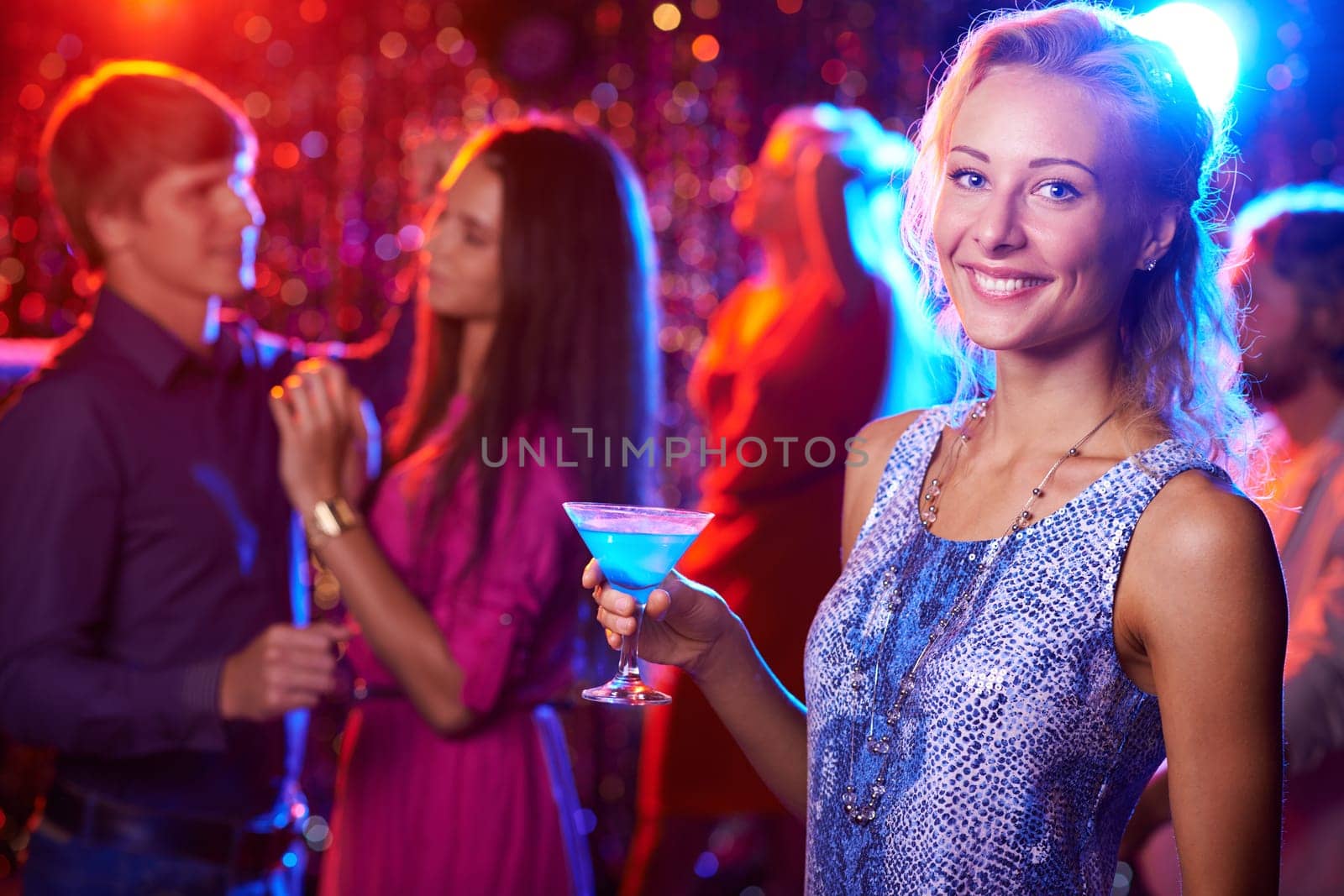 Beautiful girl posing with cocktail in nightclub, people dancing in the background