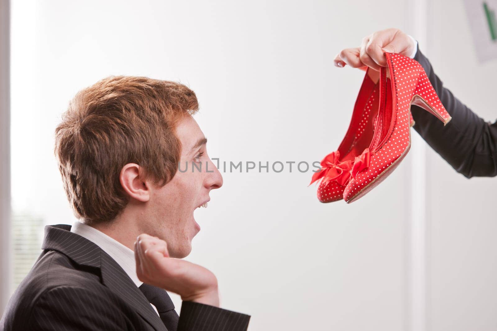 A fop boy showing an excessive happiness facing a pair of red shoes with medium heels
