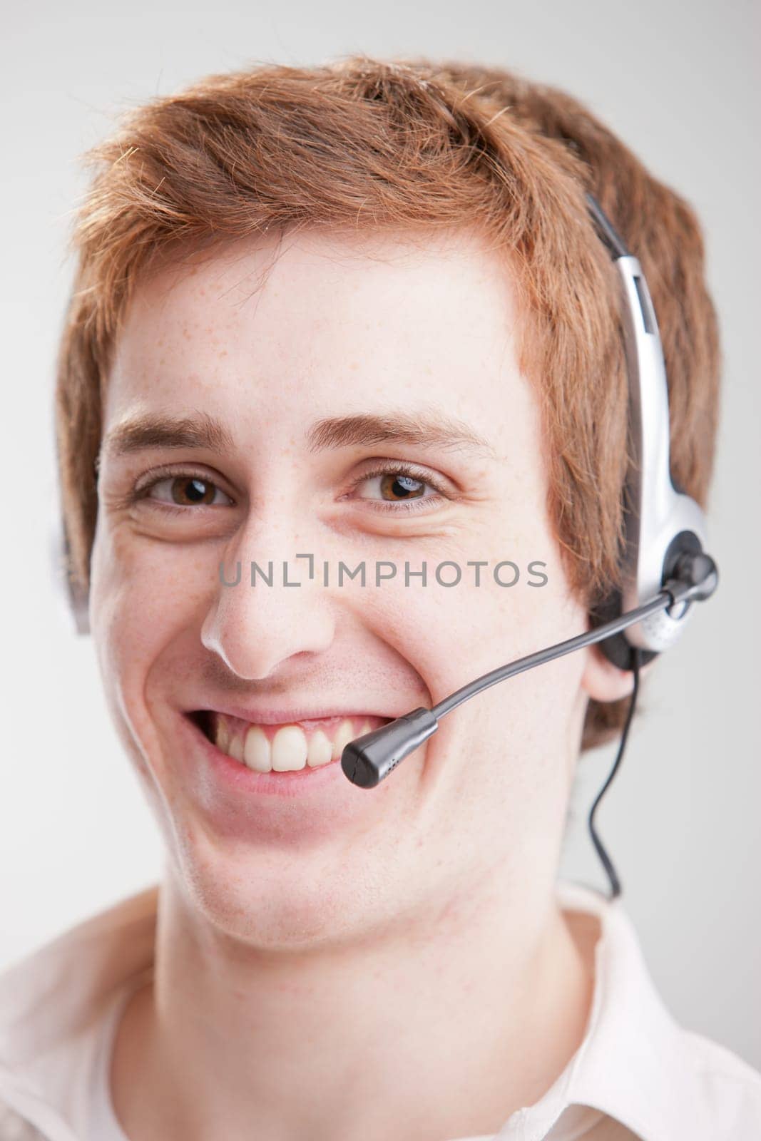 A smiling young man with red hair smiling and wearing an headset