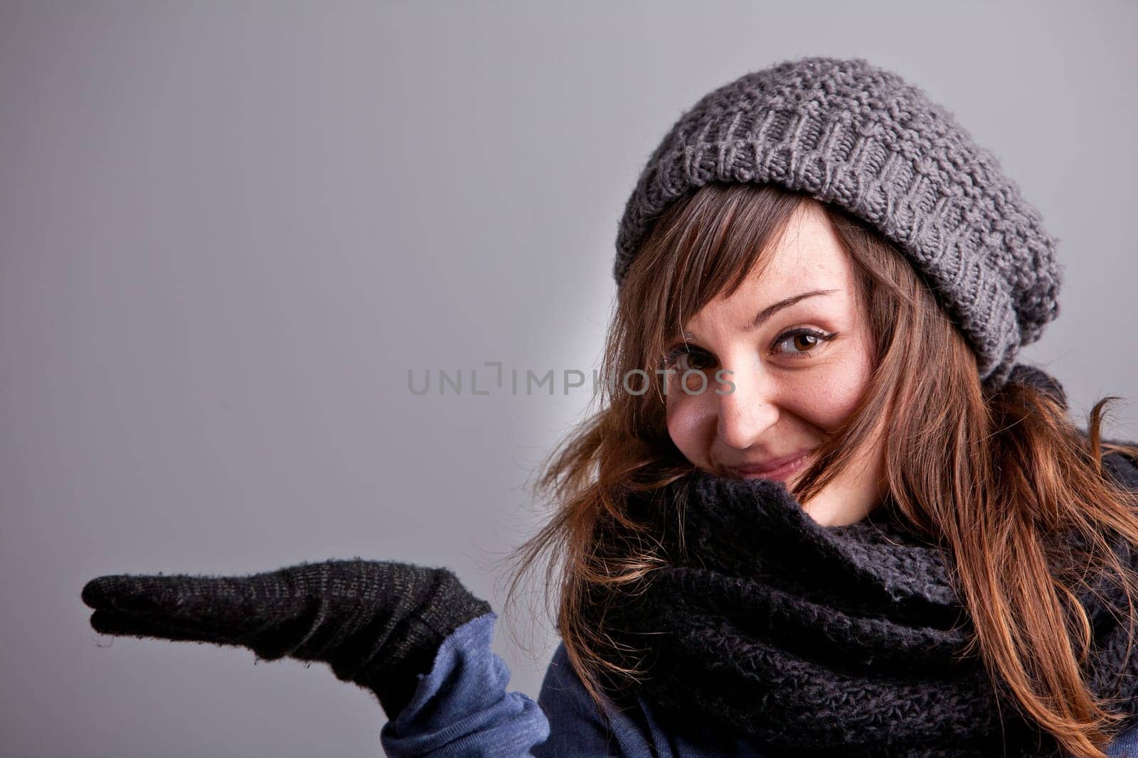 A pretty natural smiling girl in winter clothes raising her hand to show off your COPY SPACE