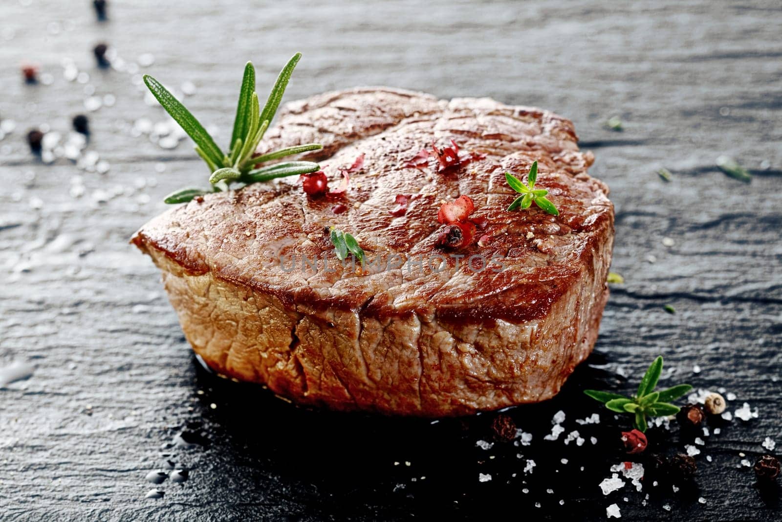Succulent thick grilled beef steak trimmed for fat for a healthy diet on a griddle with a sprig of fresh rosemary and seasoned with salt and peppercorns