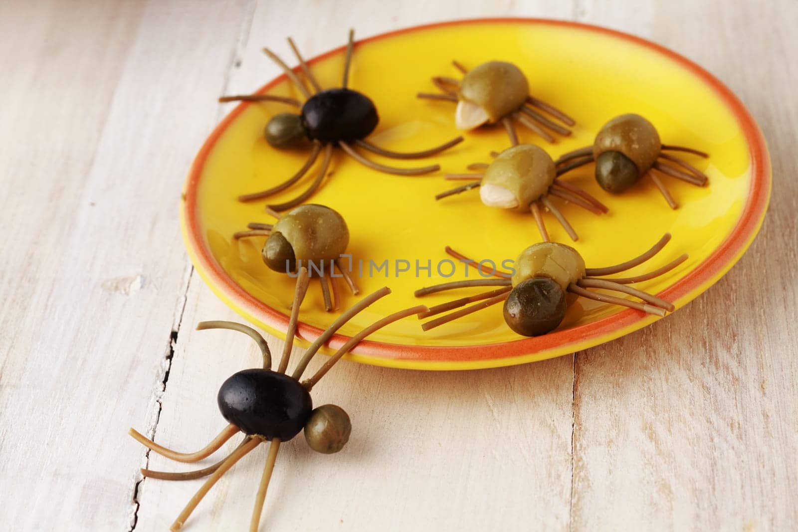 Creepy crawly Halloween spider snacks for a party celebration made from black and green olives with Italian spaghetti legs served on a yellow plate on a rustic white wooden table
