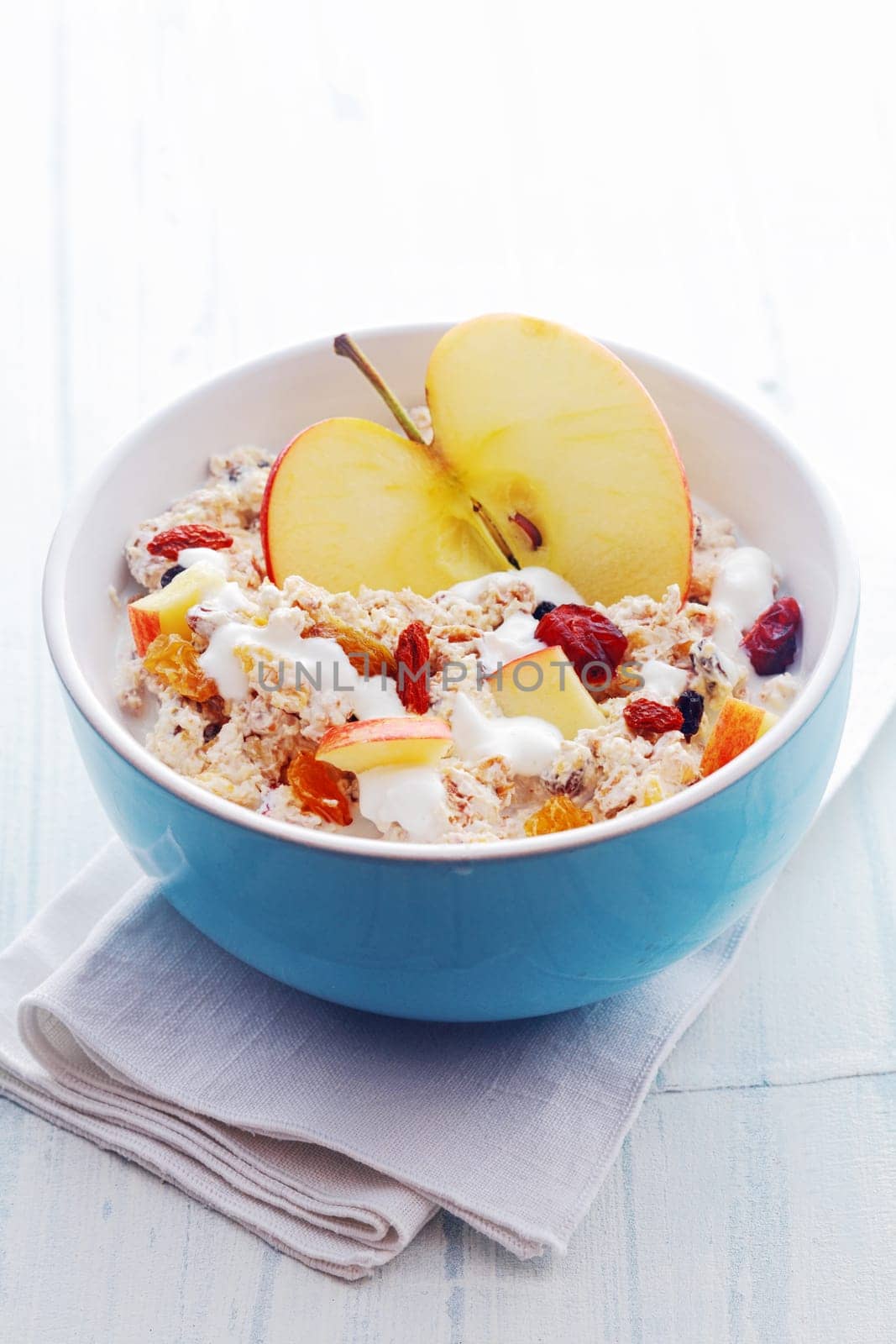 Bowl of healthy breakfast cereal with a halved fresh apple and topped with diced apple, dried fruit and nuts served with milk in a blue ceramic bowl, high angle view