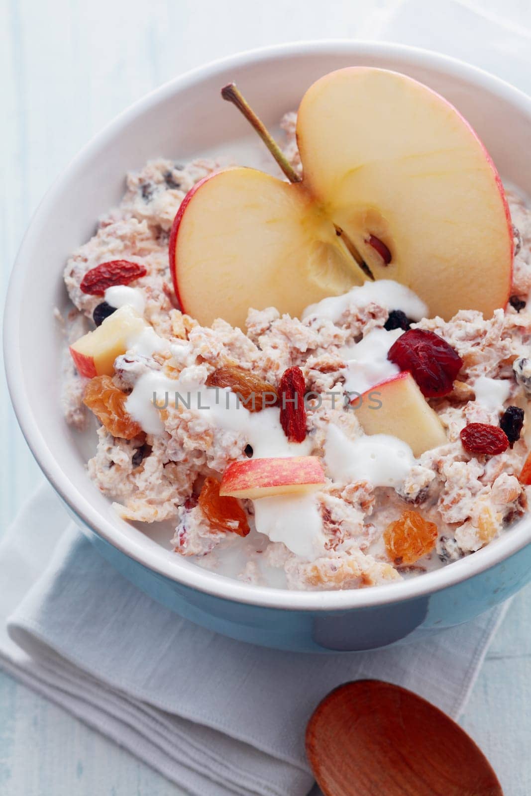 View from above of a bowl of healthy muesli with fresh apple, dried fruit and nuts served with milk for an energizing start to the day