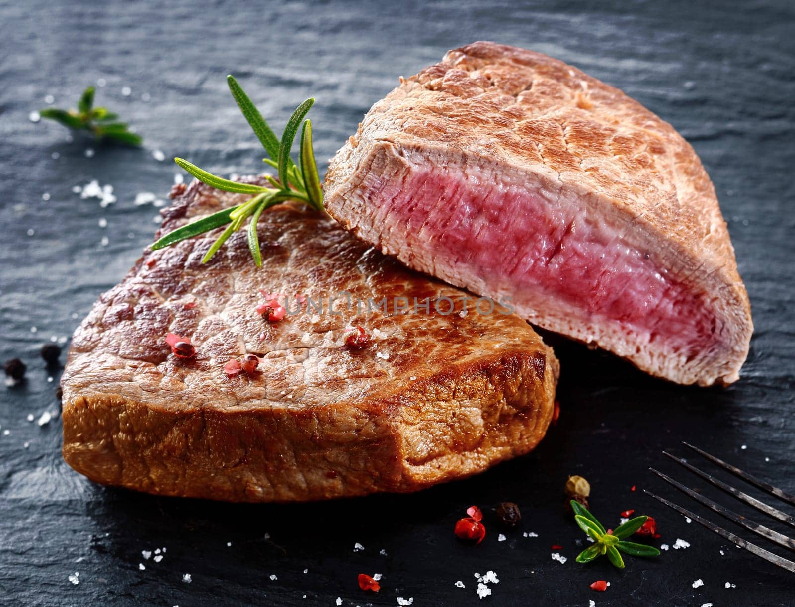 Two portions of lean trimmed grilled beef steak cut through to show the succulent tender red meat and seasoned with rosemary, salt and pepper in a steakhouse or restaurant