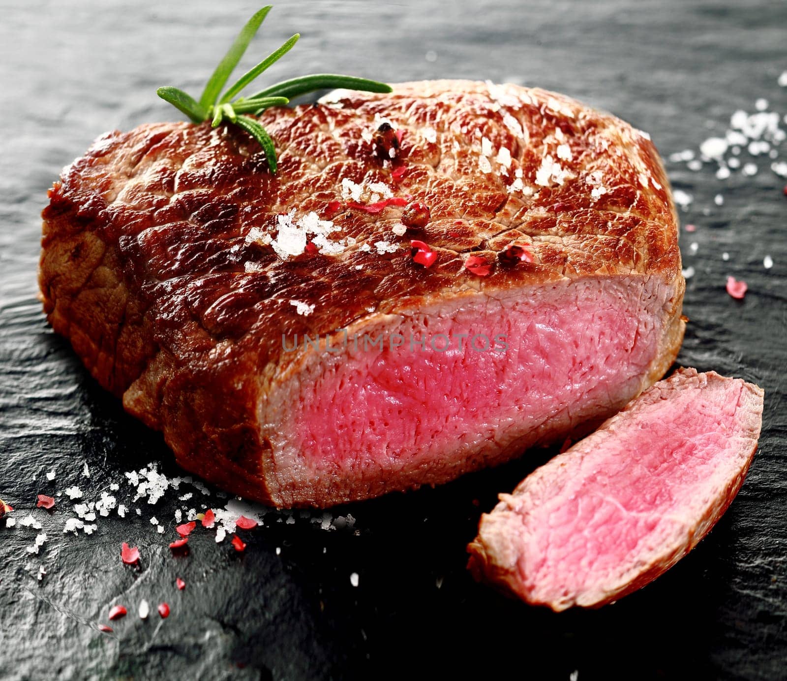 Succulent portion of rare beef steak sliced through to show the red meat and texture seasoned with salt and pepper and a sprig of fresh rosemary, closeup view showing the texture of the cut surface