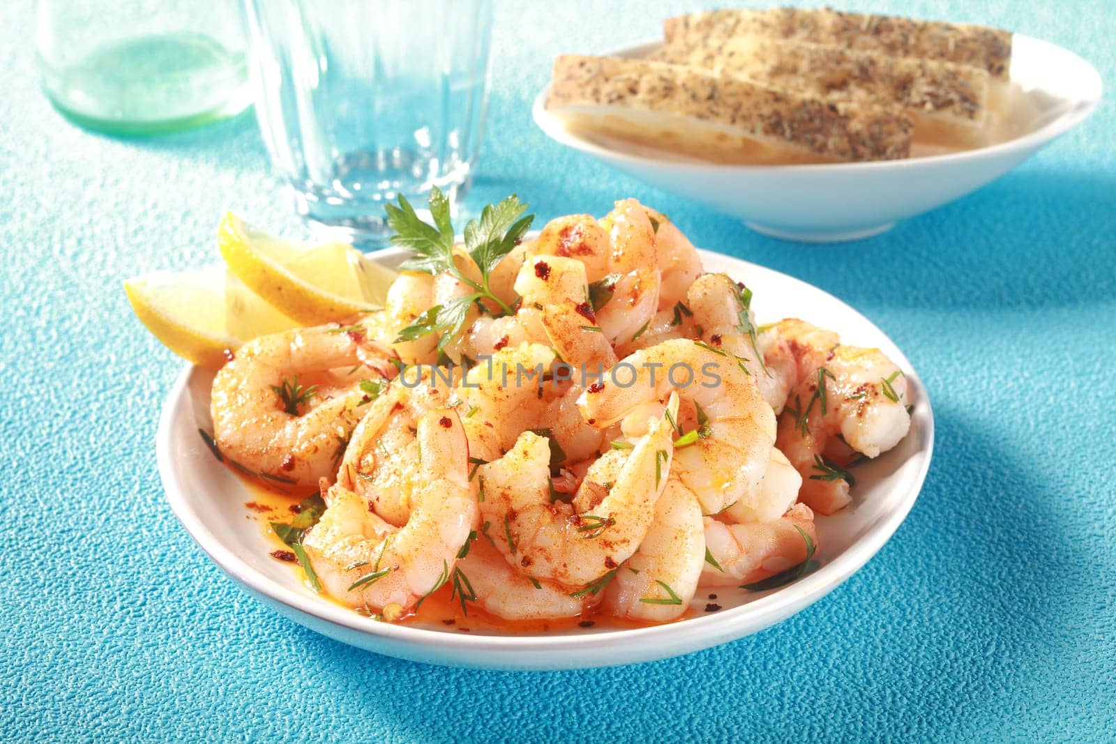 Gourmet seafood starter of grilled pink prawns or shrimps seasoned with fresh herbs and olive oil and garnished with fresh lemon slices on a blue table